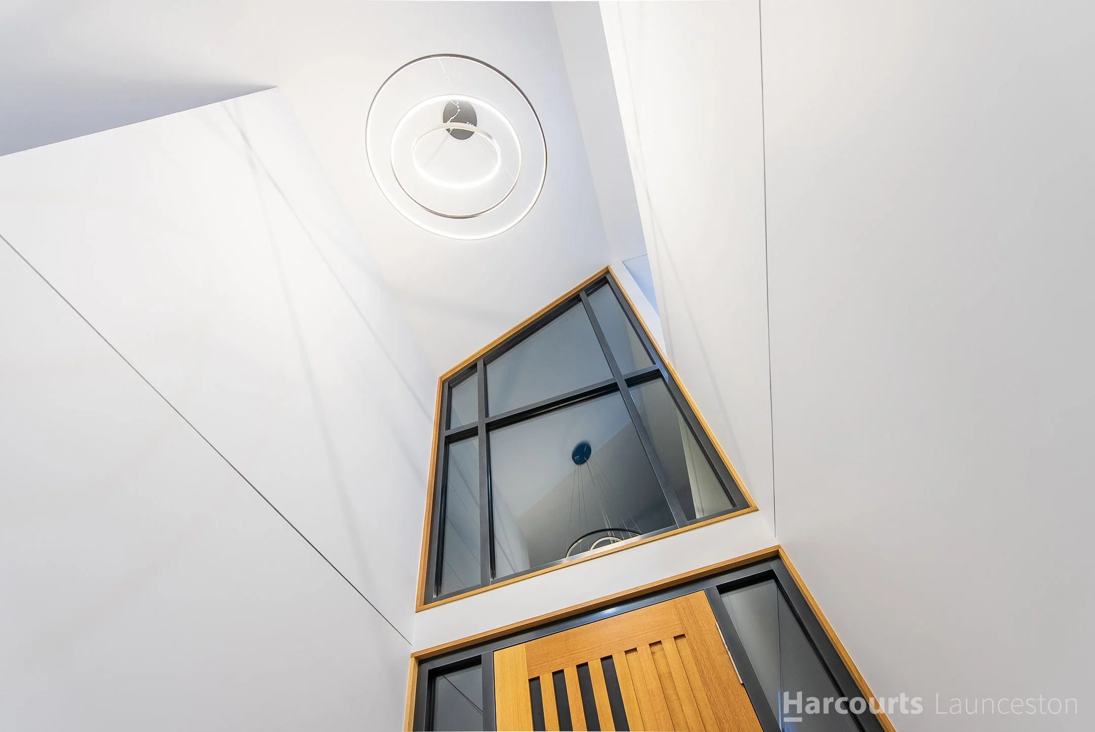 Interior view of a modern building with a curved white ceiling, a circular light fixture, and a black-framed glass window with a wooden border.
