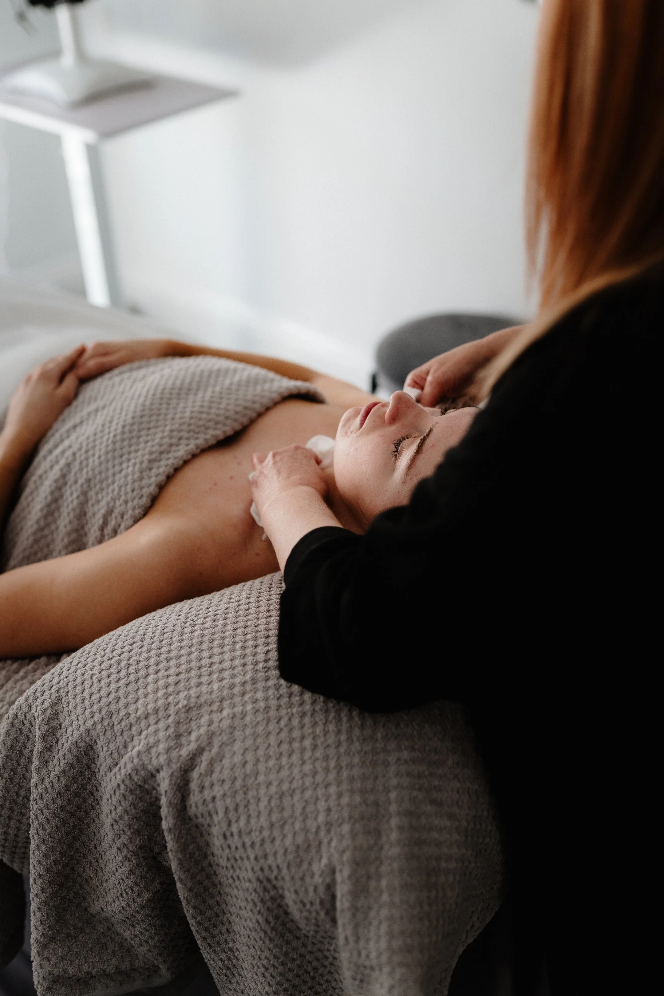 A woman receiving a facial massage from an aesthetician in a spa or clinic setting.