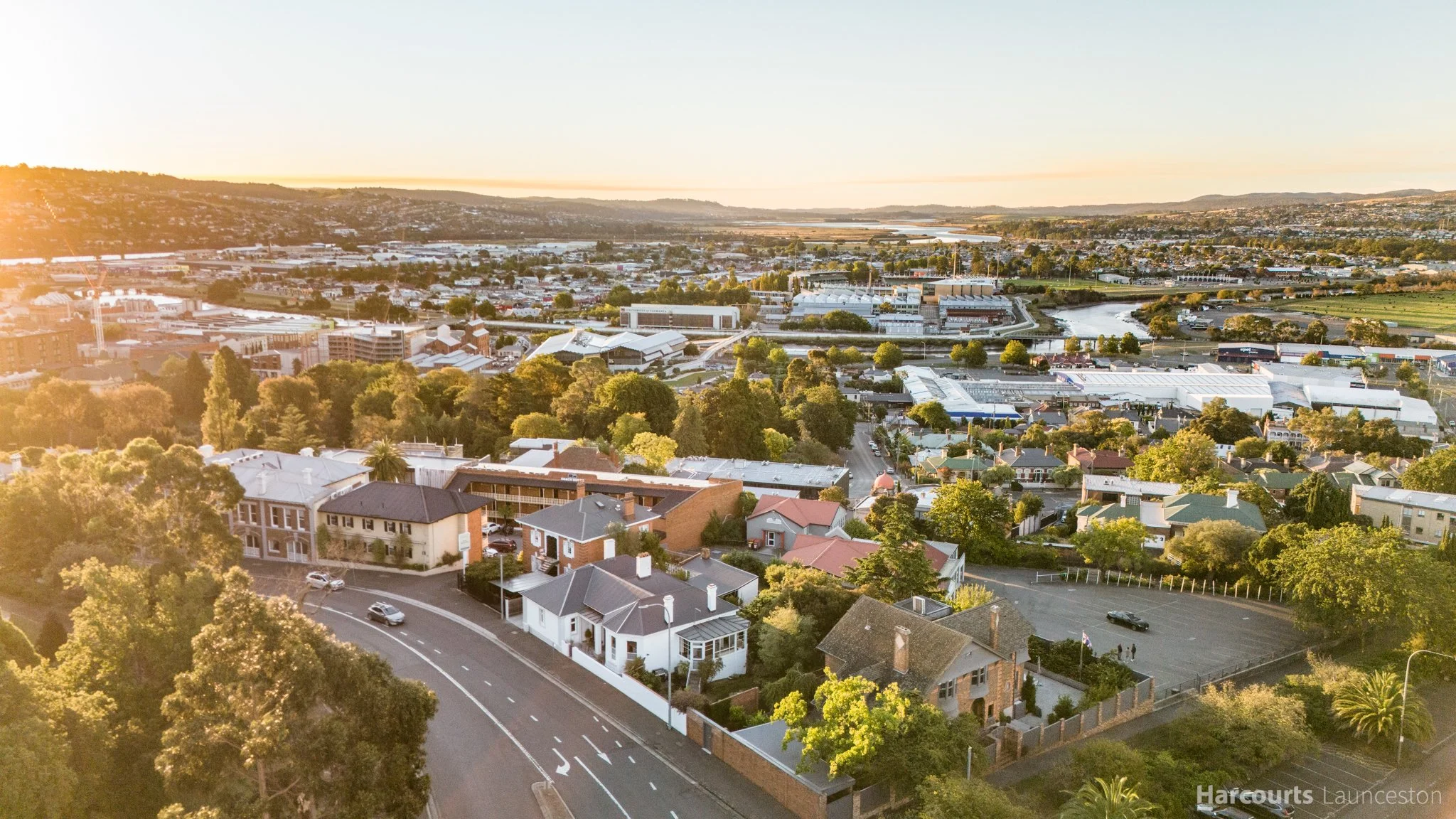 Aerial view of a city during sunset with greenery, houses, buildings, and a river.