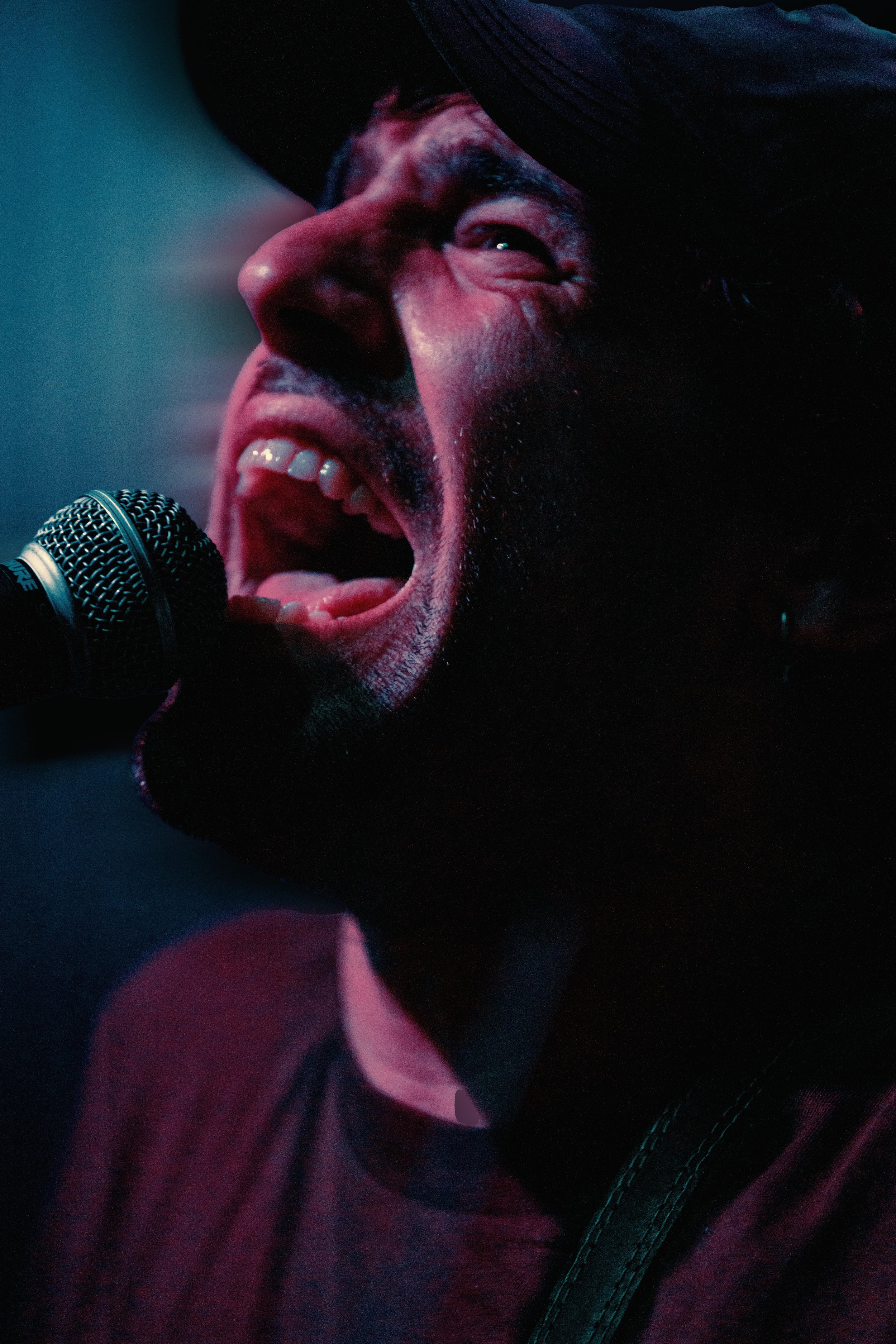 A close-up of a person singing or shouting into a microphone, with a dark background and dramatic lighting.