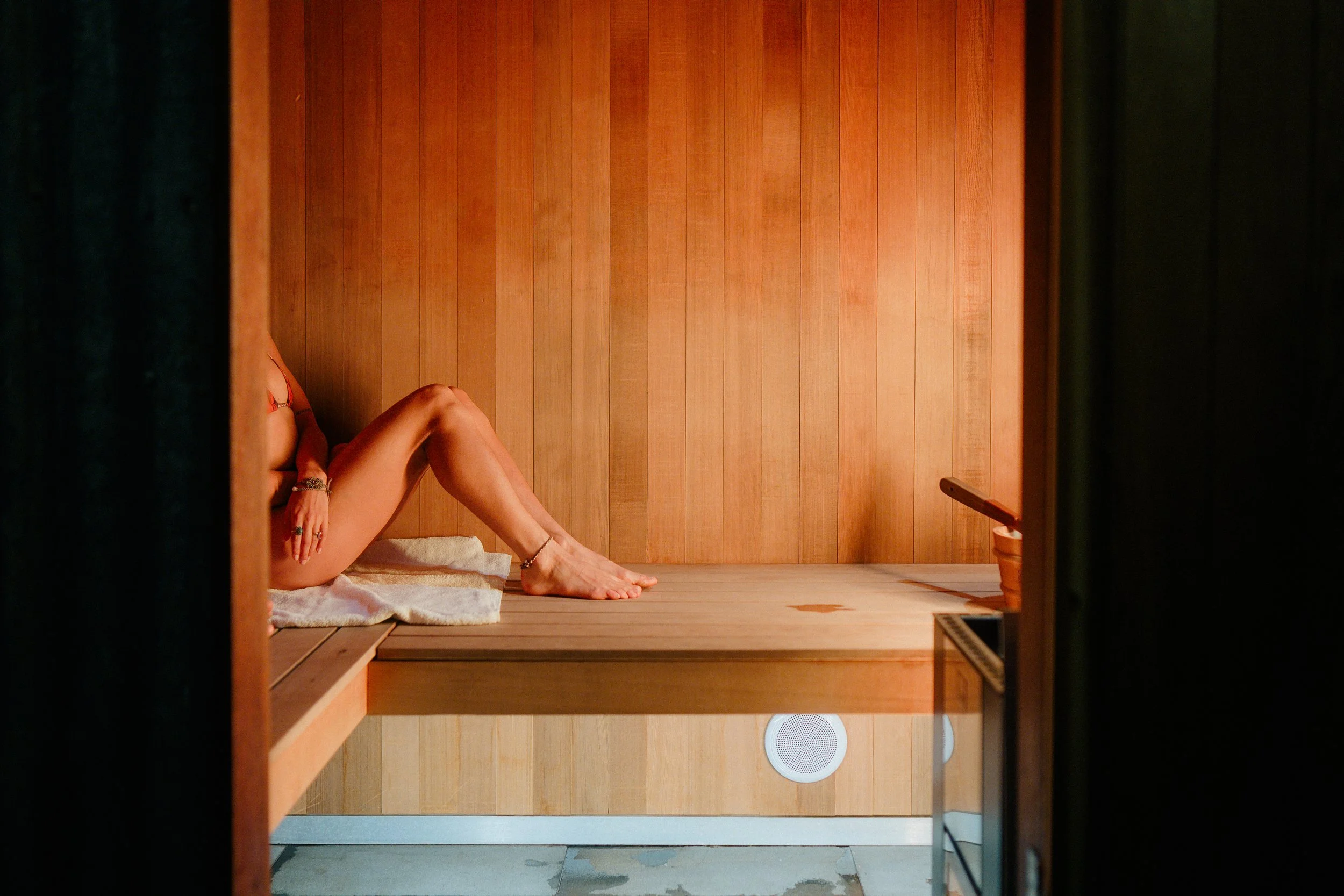 A person lying in a sauna with their legs bent at the knees, with a towel underneath them, and the sauna walls are made of wood.