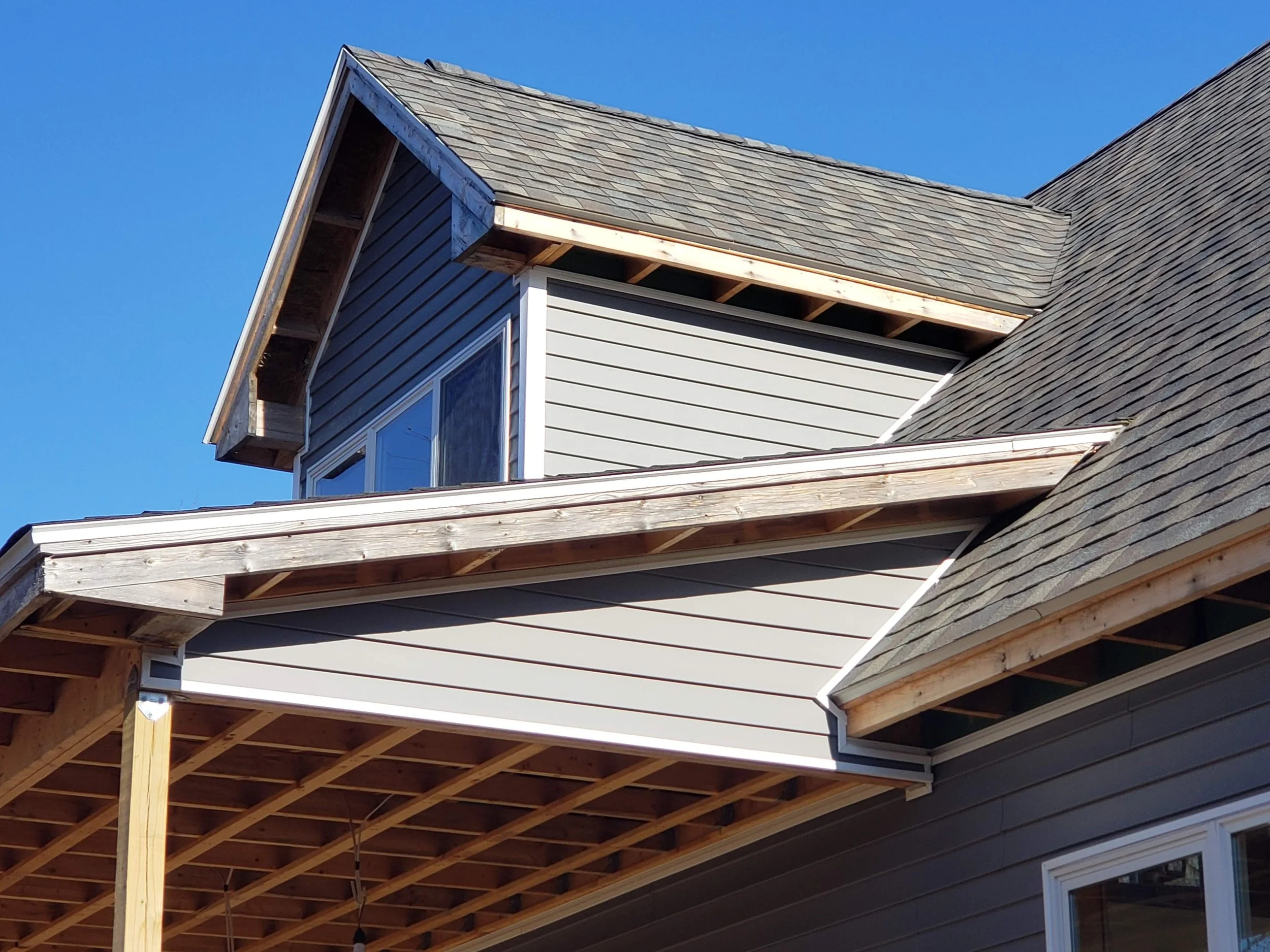 The image shows the roof of a house under construction. The roof has a combination of shingles and some areas where the roofing framework is exposed, with wooden beams visible.