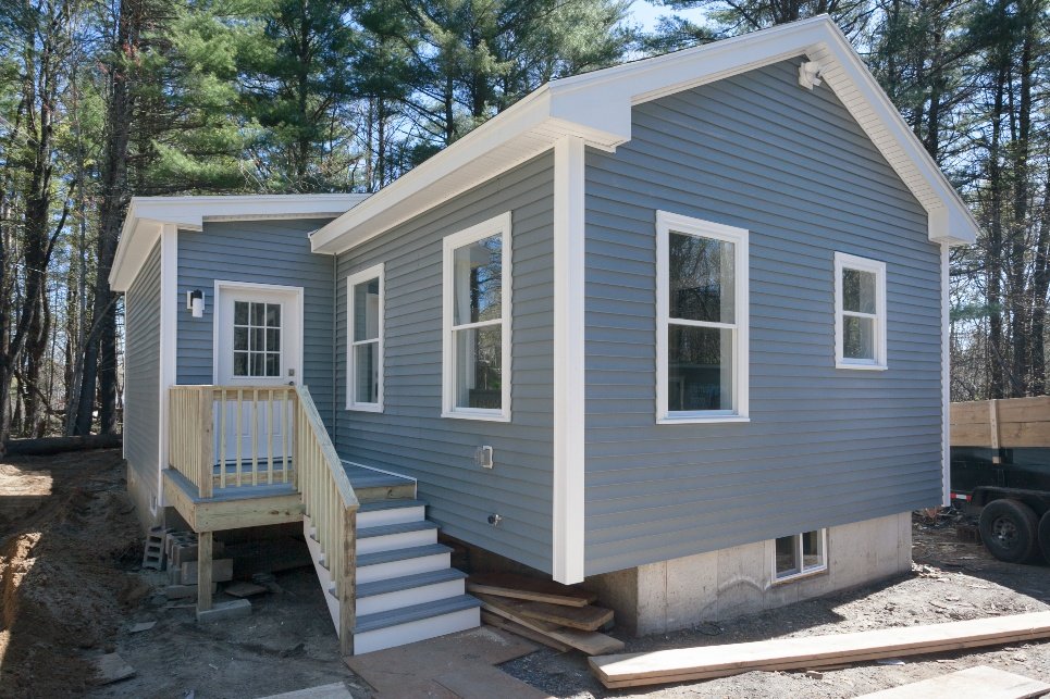 New gray house with white trim and small front porch with steps, surrounded by trees.