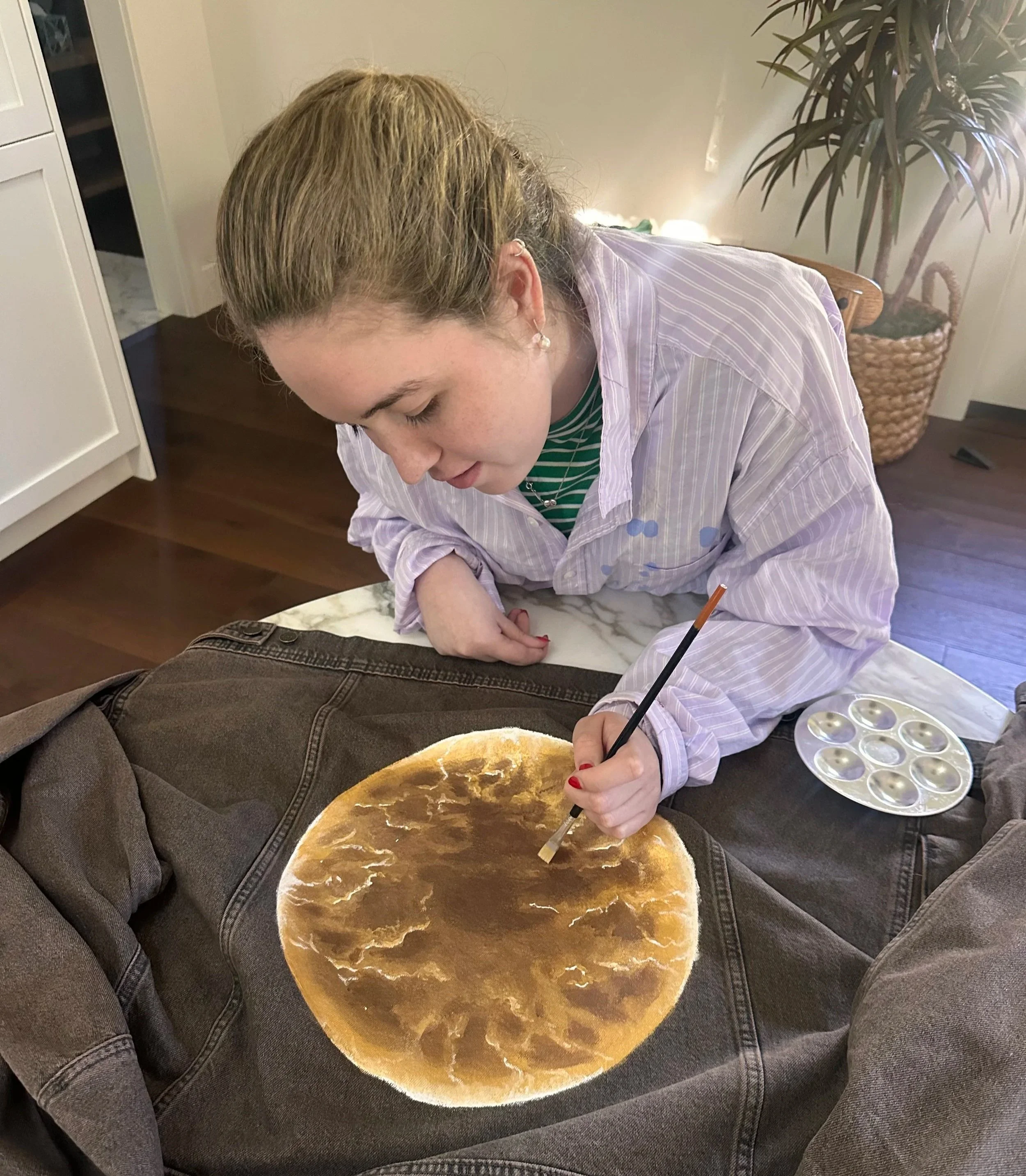 Elle sitting at a table, painting a moon onto a denim jacket