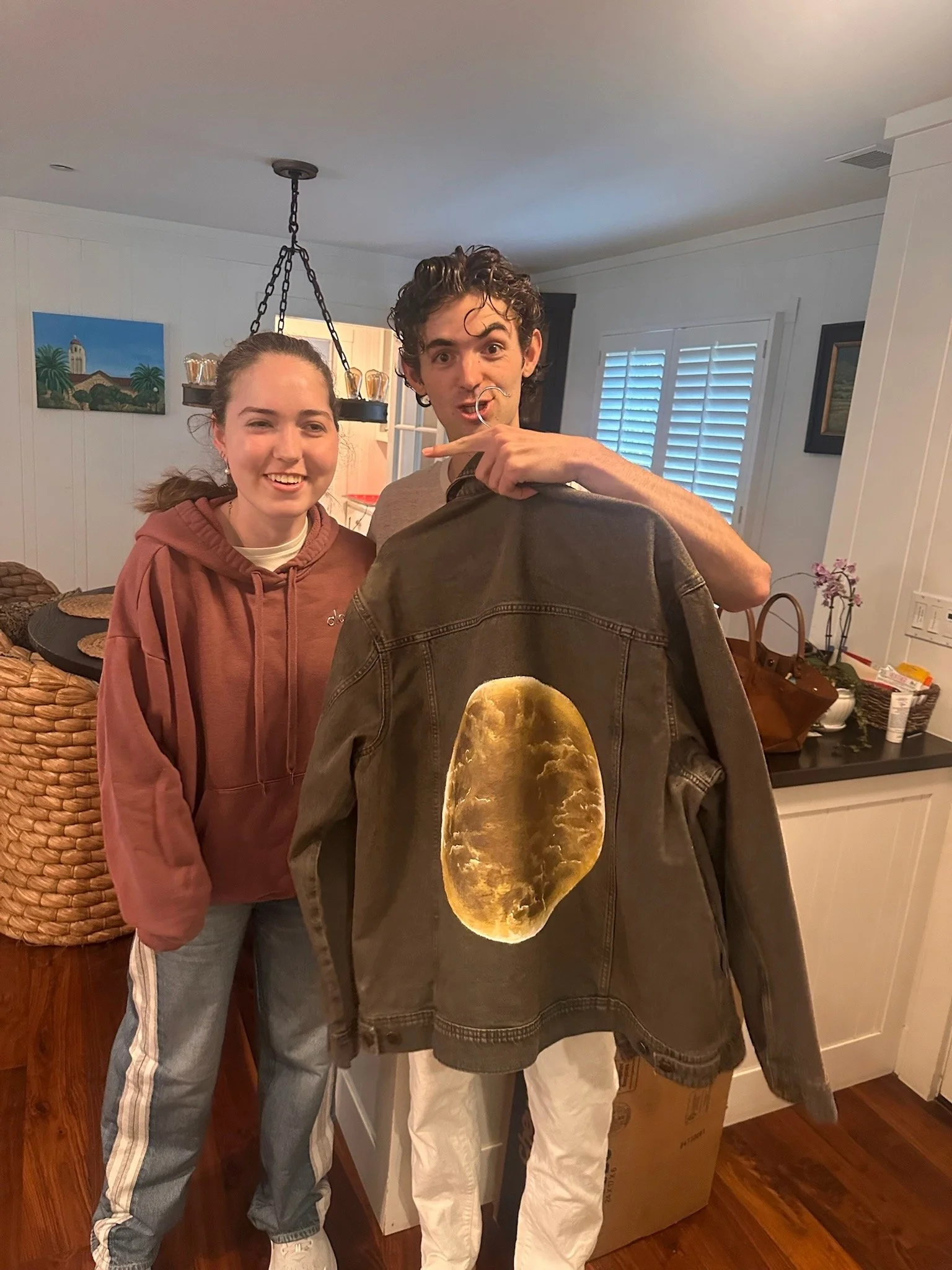 Elle and a young man standing,  holding a jacket that has a moon printed on the back.