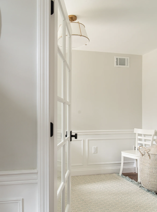 Part of a bright, modern living room with white walls, wainscoting, and a white chair.