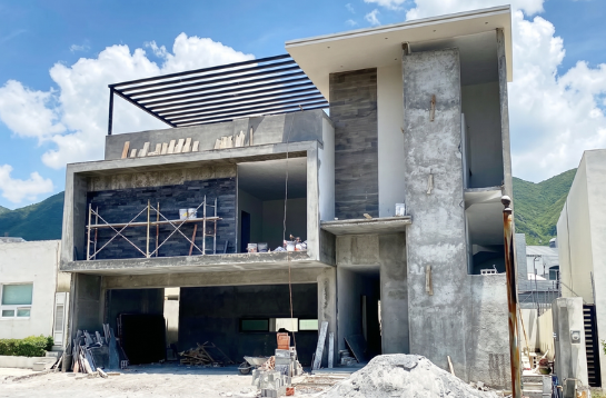 Edificio en construcción con estructura de concreto y madera, en un entorno montañoso.