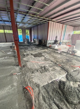 Espacio de construcción con suelo en preparación, cables y herramientas, estructura de metal y pared de lámina en el fondo.
