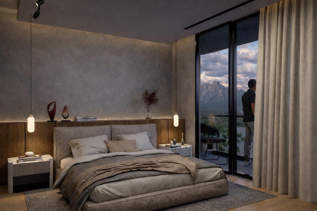 Habitación moderna con cama, dos mesitas de noche con objetos decorativos y libros, ventana grande con vista a montañas y un hombre de espaldas en el balcón.