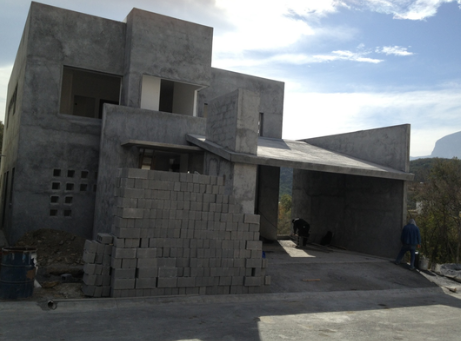 Construcción de una casa de concreto en proceso con paredes altas y pilas de bloques apilados en el frente.