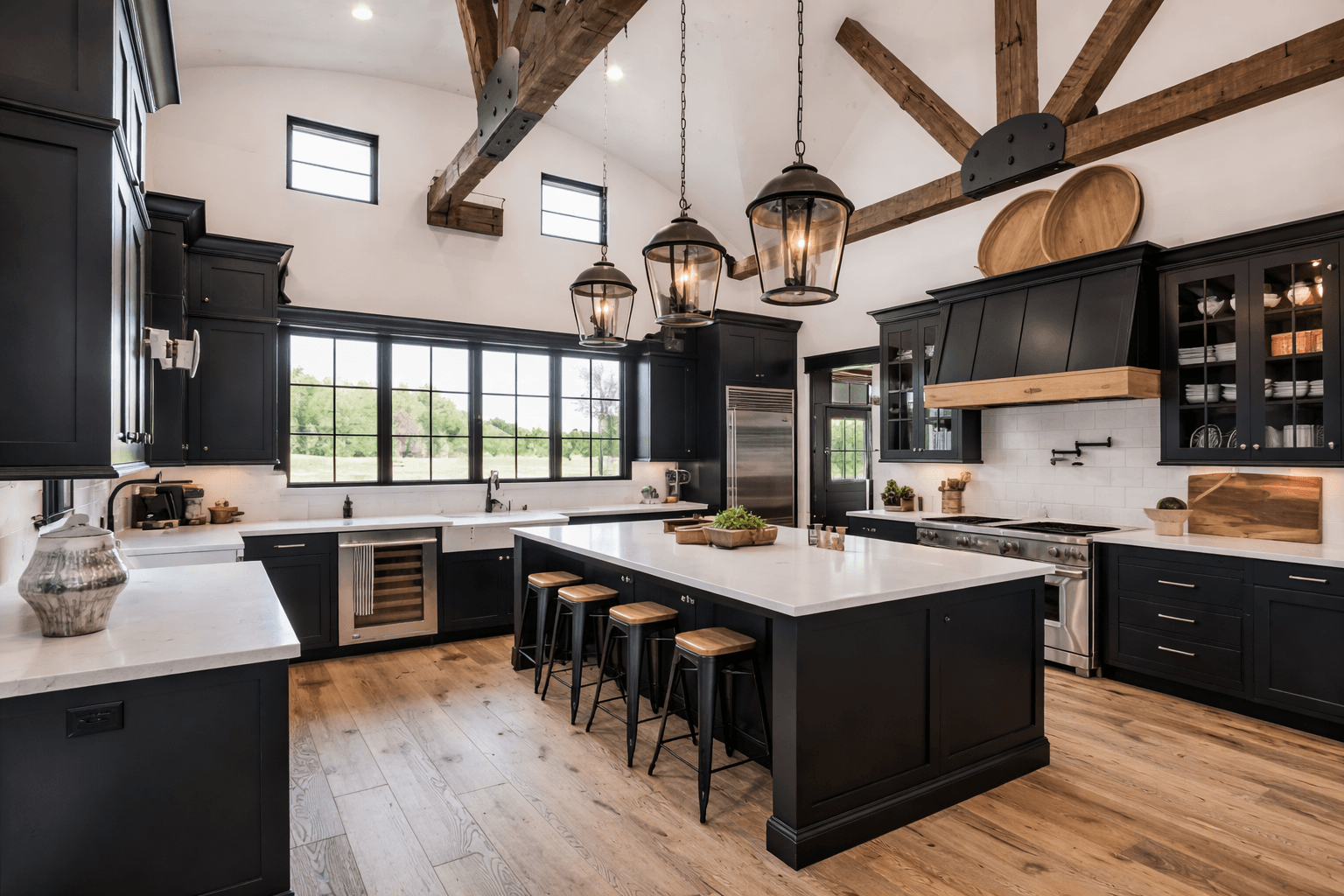 Modern kitchen with black cabinets, white countertops, wooden flooring, and rustic ceiling beams. Features large windows, pendant lights, and a center island with stools.