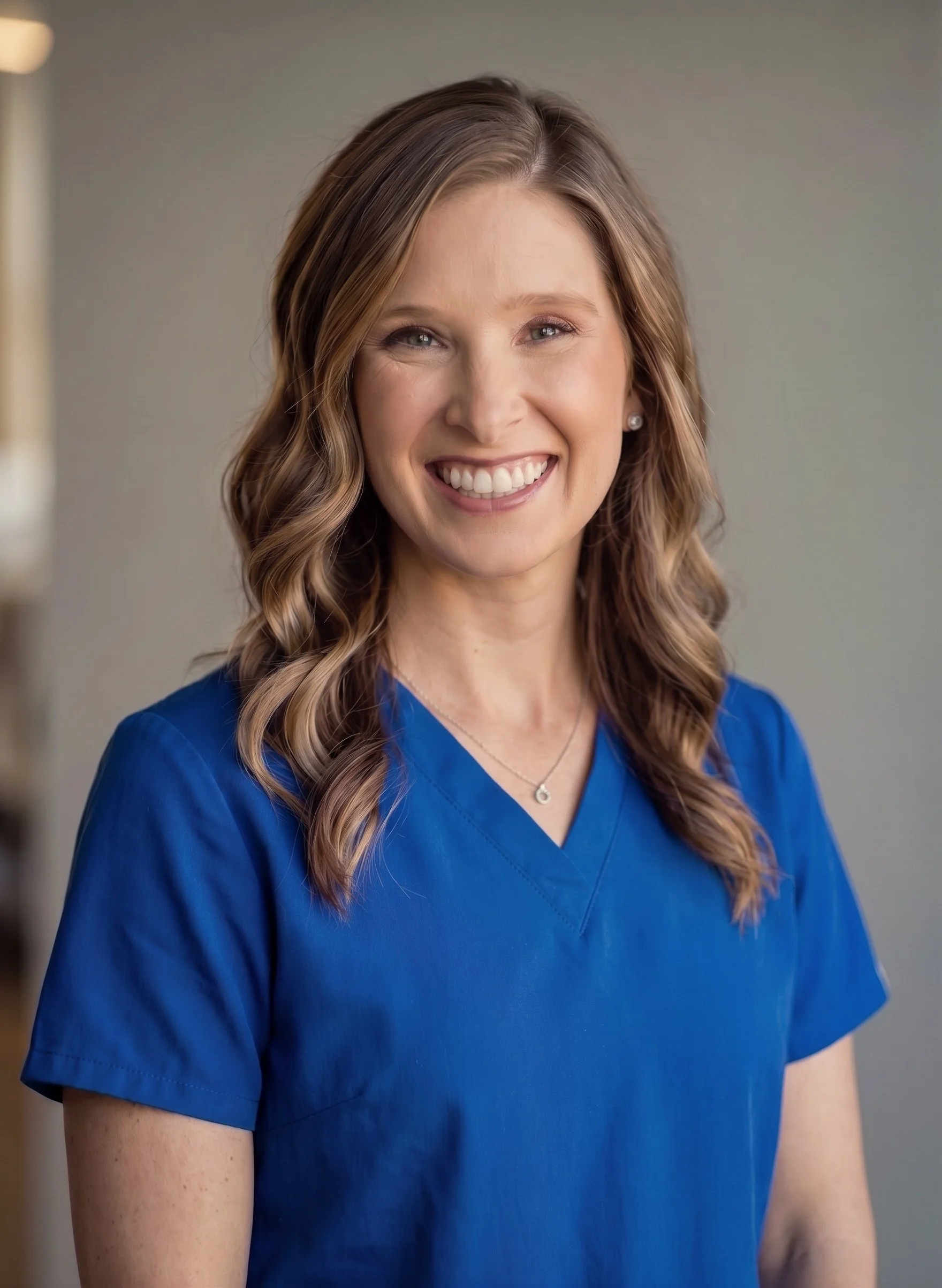 A woman wearing blue scrubs smiling at the camera.