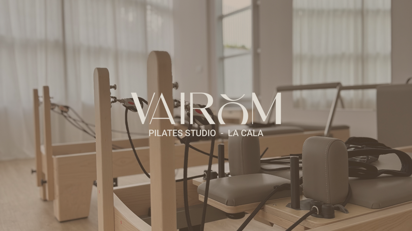 Sala de estudio de Pilates con máquinas de madera y ventanas con cortinas blancas.