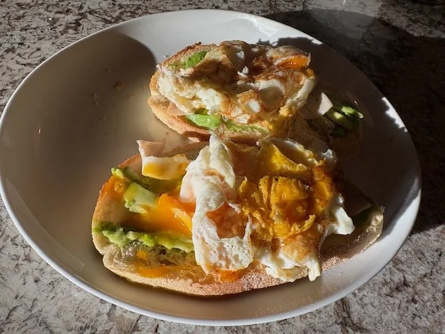 Two slices of bread with fried eggs, avocado, and possibly other vegetables on a white bowl.