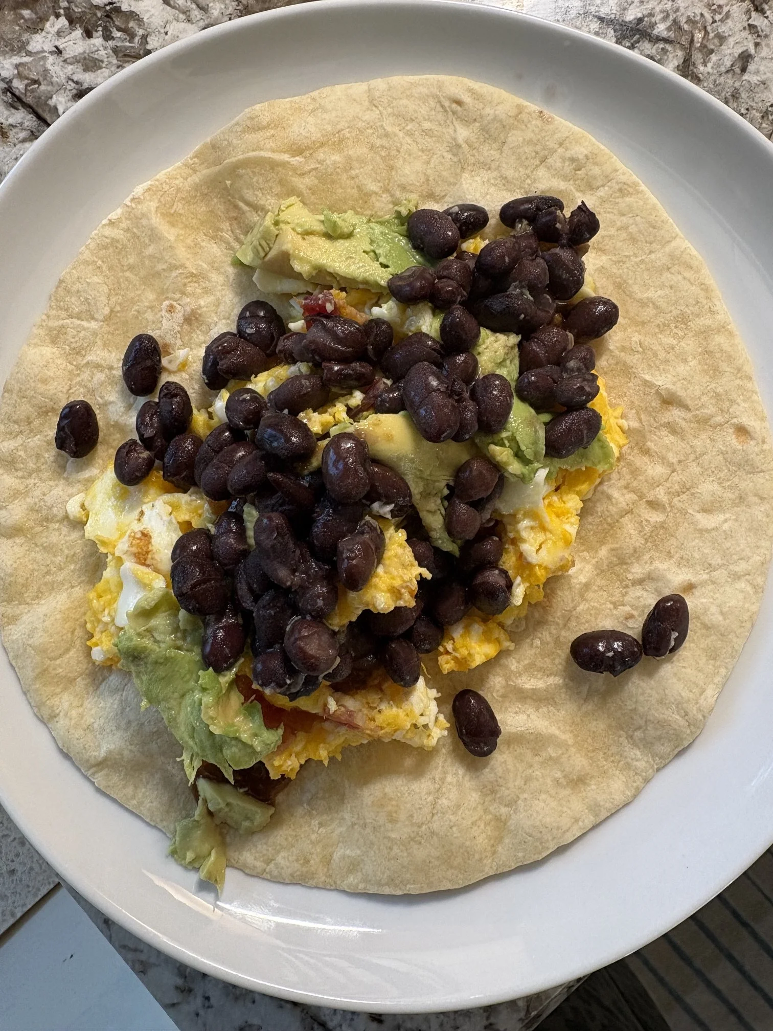 A breakfast taco on a white plate with scrambled eggs, avocado, lettuce, and black beans.