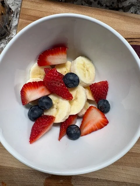 Sliced strawberries, blueberries, and banana slices in a white bowl