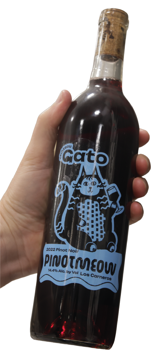 Hand holding a bottle of 2022 Pinot Noir wine named 'Pinatneou,' featuring a cartoon cat illustration on the label.