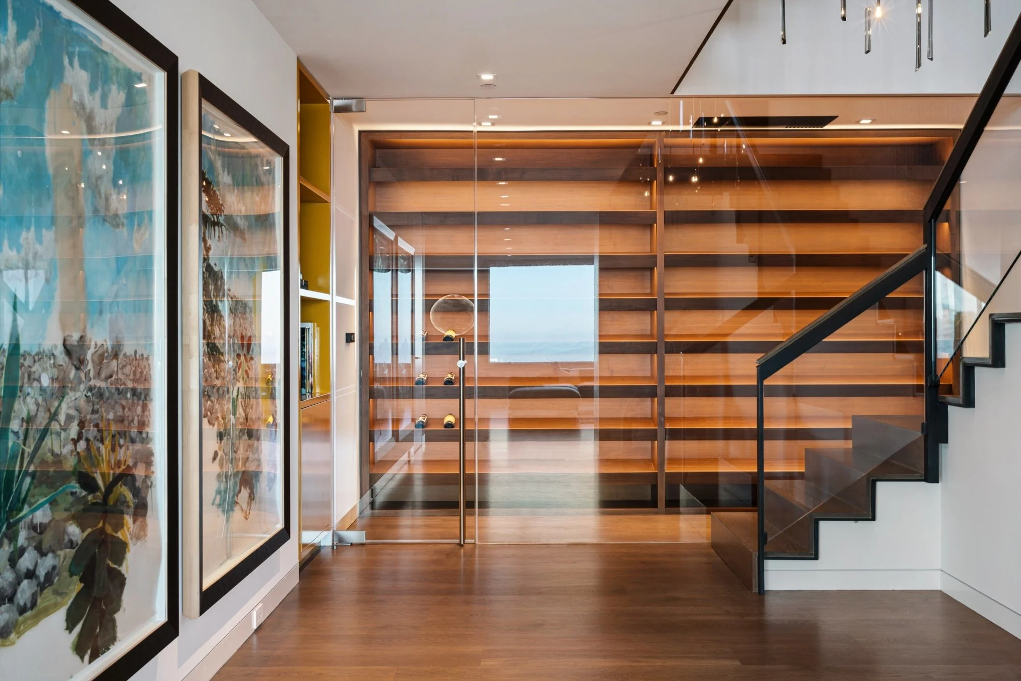 Modern interior featuring wooden staircase, glass panels, and large abstract paintings on the wall.