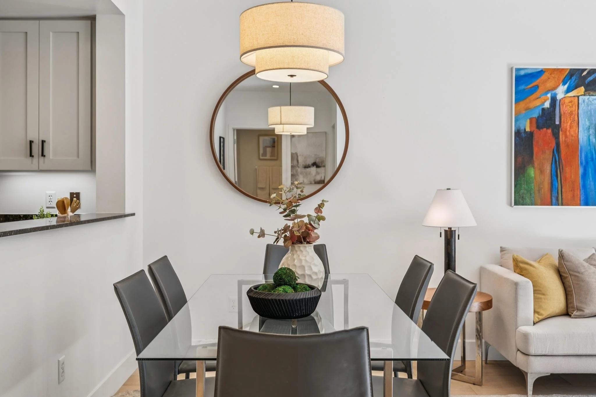 Interior of a modern apartment with a dining area, living room with large windows and seating, and a partial view of the kitchen.