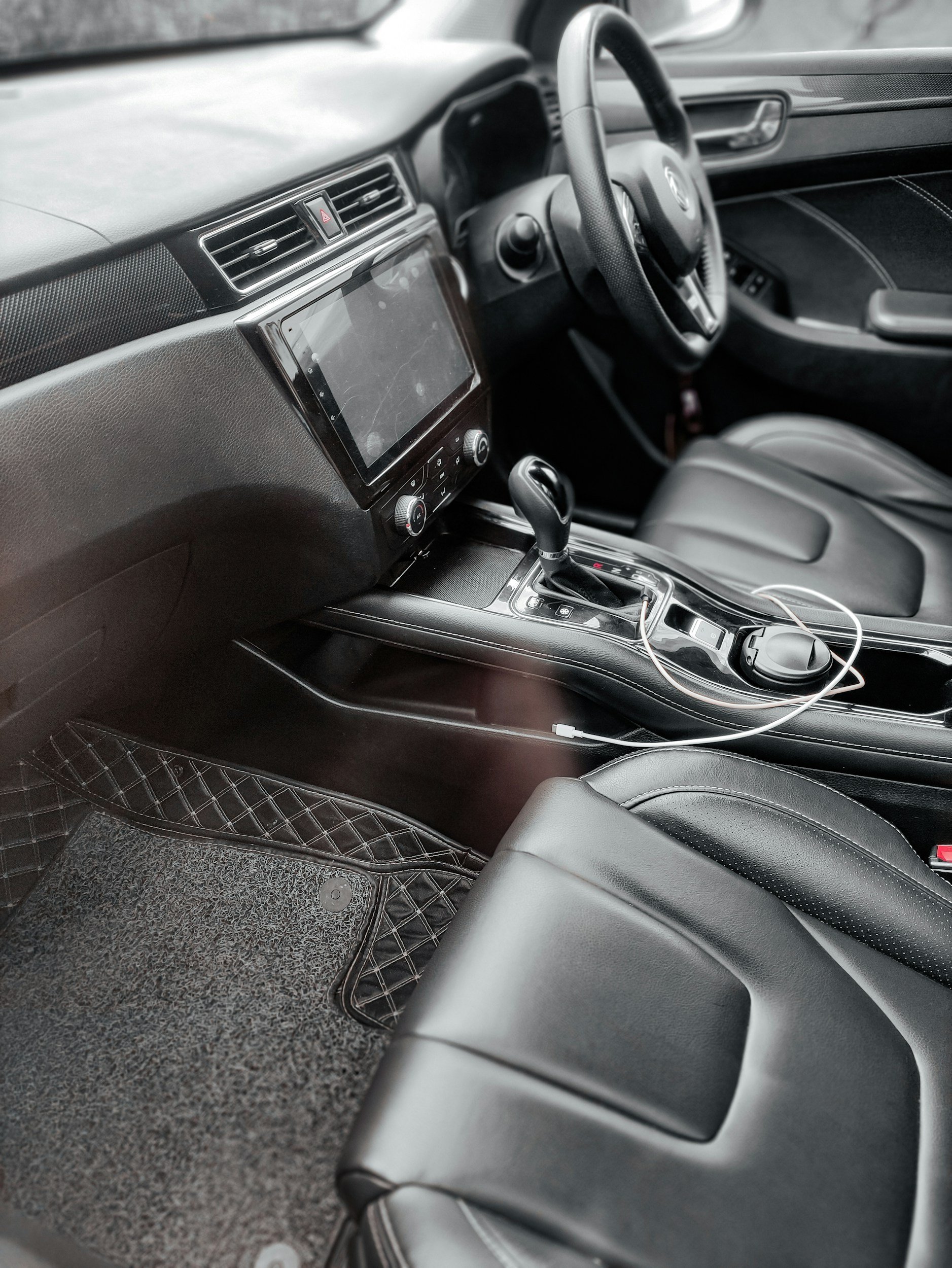 Interior of a car showing the dashboard, steering wheel, center console with gear shift, touchscreen display, air vents, and part of the front passenger seat and floor mat.