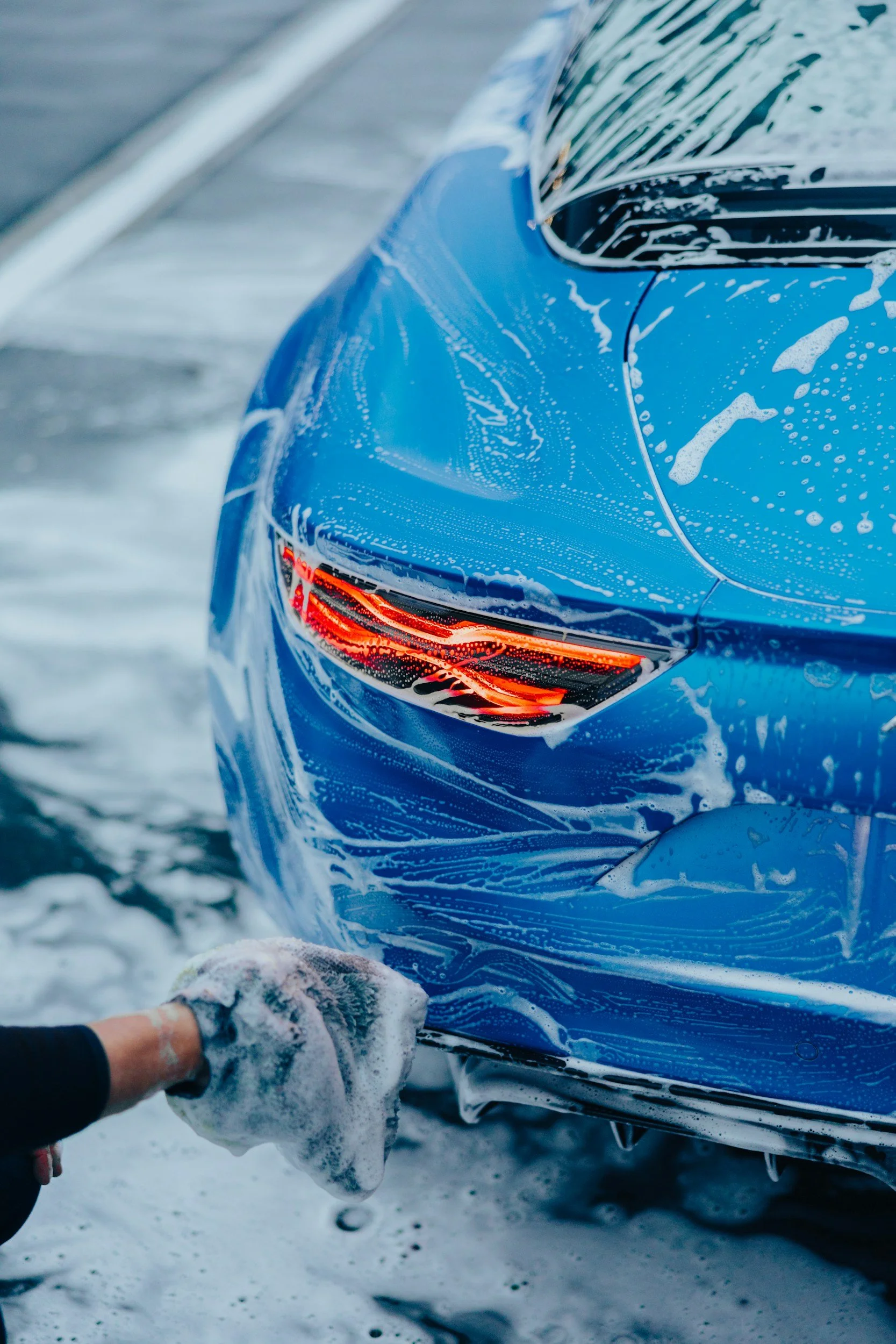 A person washing a blue car with soap and water in a snowy outdoor setting.