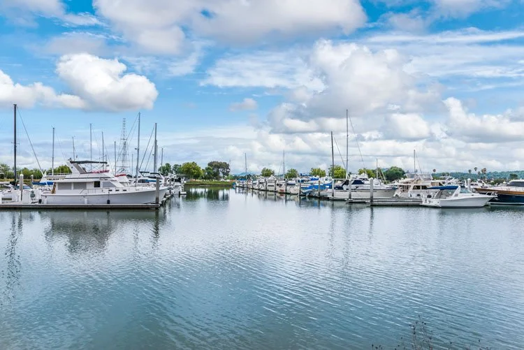 Marina with various sailboats and yachts docked on calm water under a partly cloudy sky.