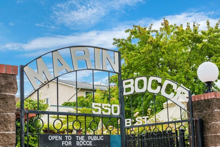 Entrance gate with the words Marine View and Bocce, 550 B St, open to the public for bocce, with trees and a blue sky in the background.