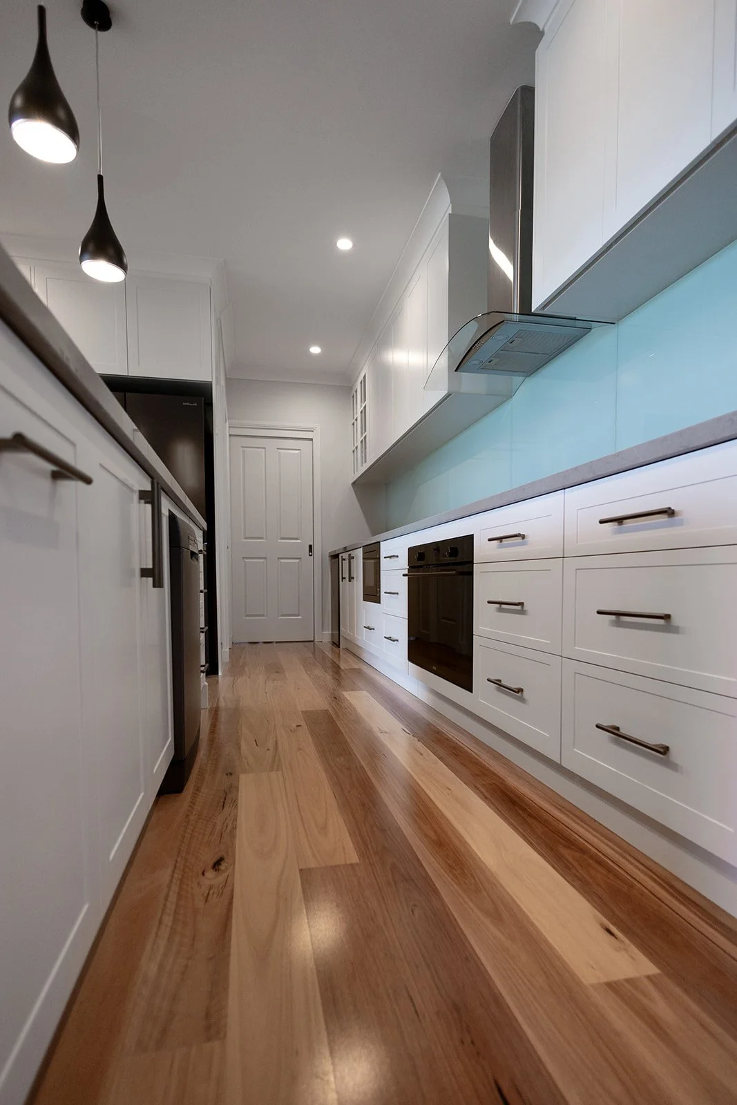A modern kitchen with white cabinets, stainless steel appliances, and hardwood floors. Pendant lights and recessed ceiling lights.