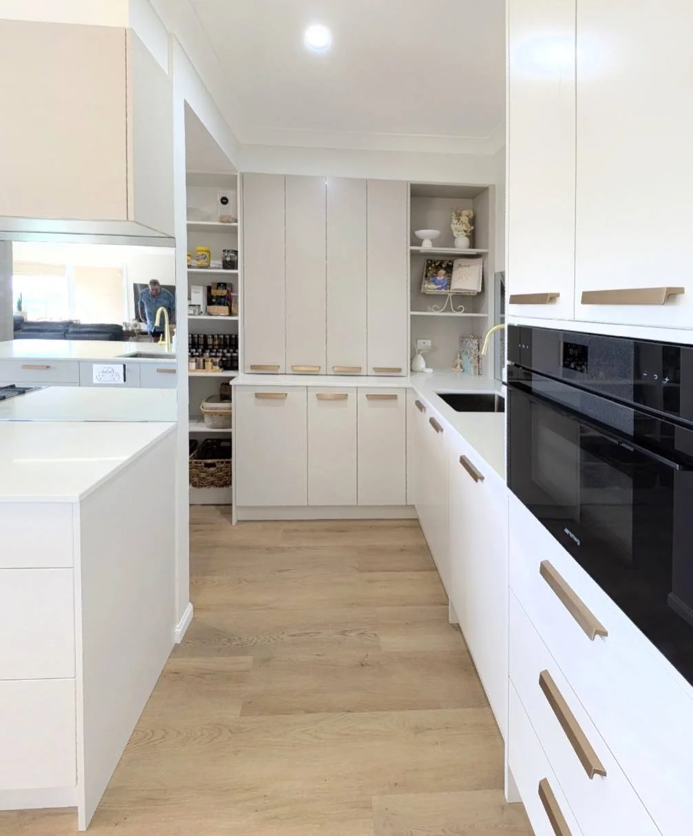 Modern kitchen with white cabinets, black built-in oven, and light wood flooring.