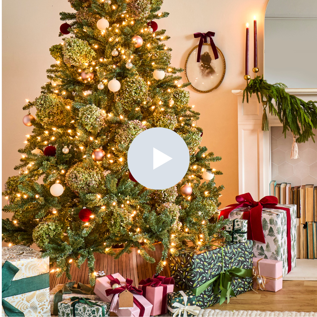 Decorated Christmas tree with lights and ornaments, surrounded by wrapped presents with bows, in a cozy room with stockings and greenery