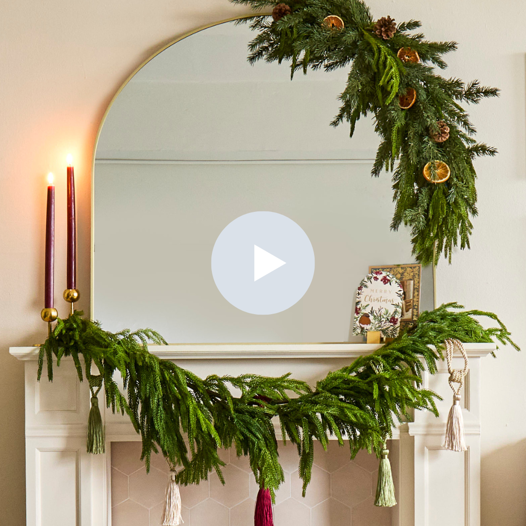 Decorated fireplace mantel with a mirror, green garland with dried orange slices, candles, and holiday cards.