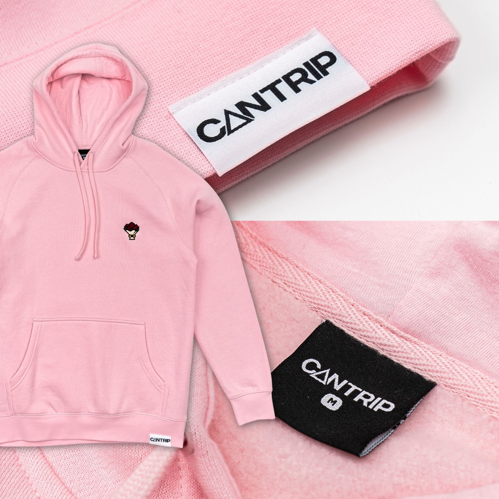 Pink hoodie with small embroidered graphic of a character wearing glasses and a crown, placed on a pink textured fabric surface with a white tag labeled "CAN TRIP."