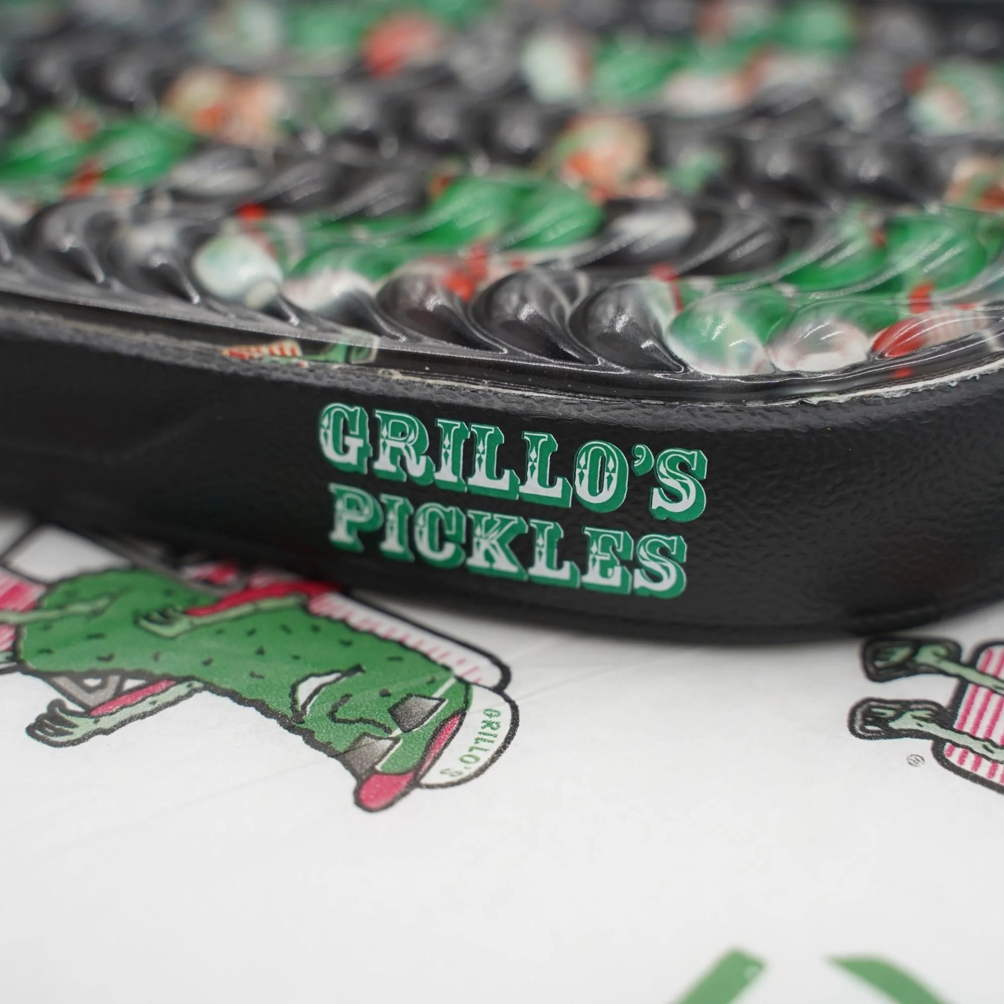 Close-up of black pool slides with a pickle pattern printed on the insole and a Grillo's Pickle logo on the side.