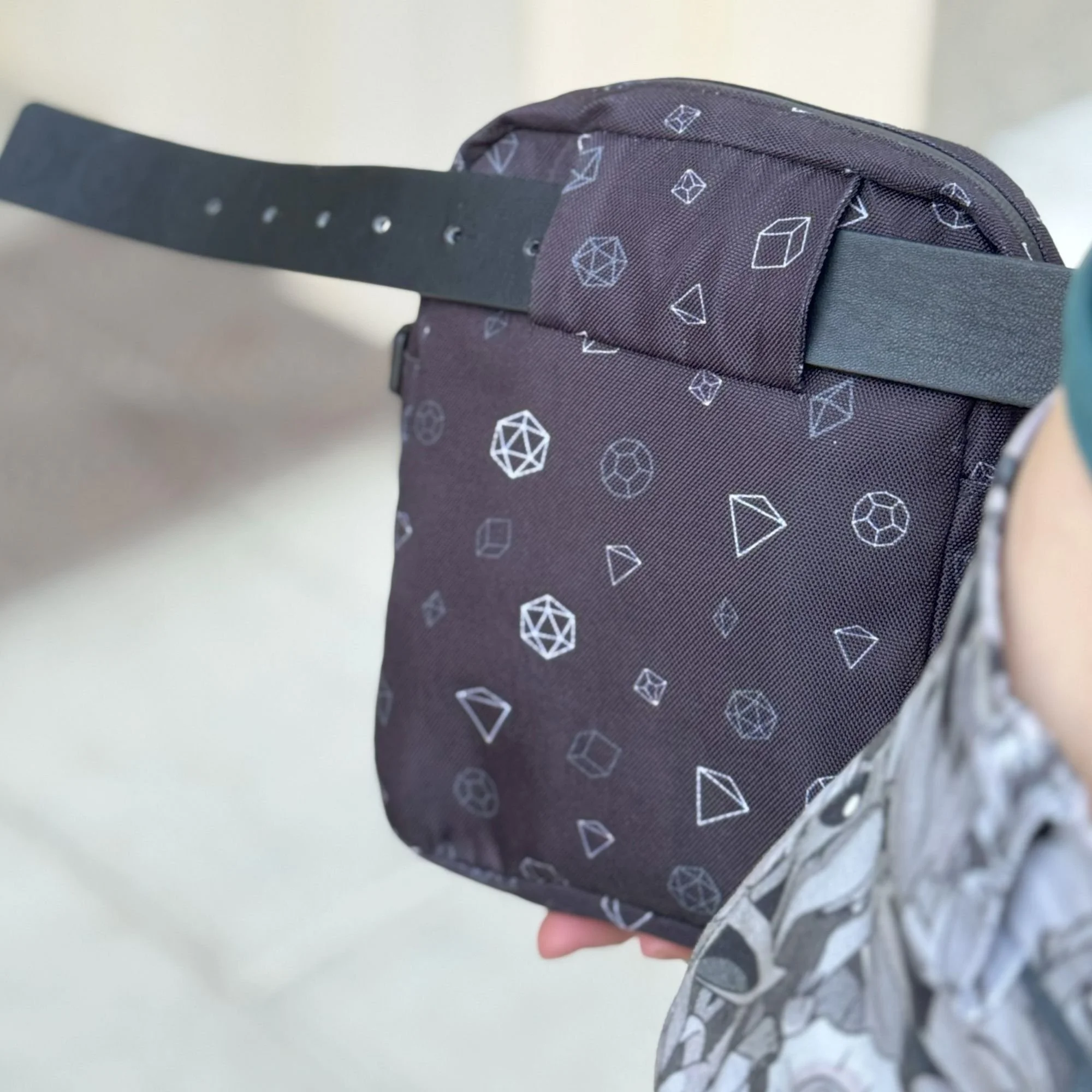 A close-up of a person holding a small purple backpack with white geometric patterns, wearing a gray long-sleeve shirt and a striped wristwatch.