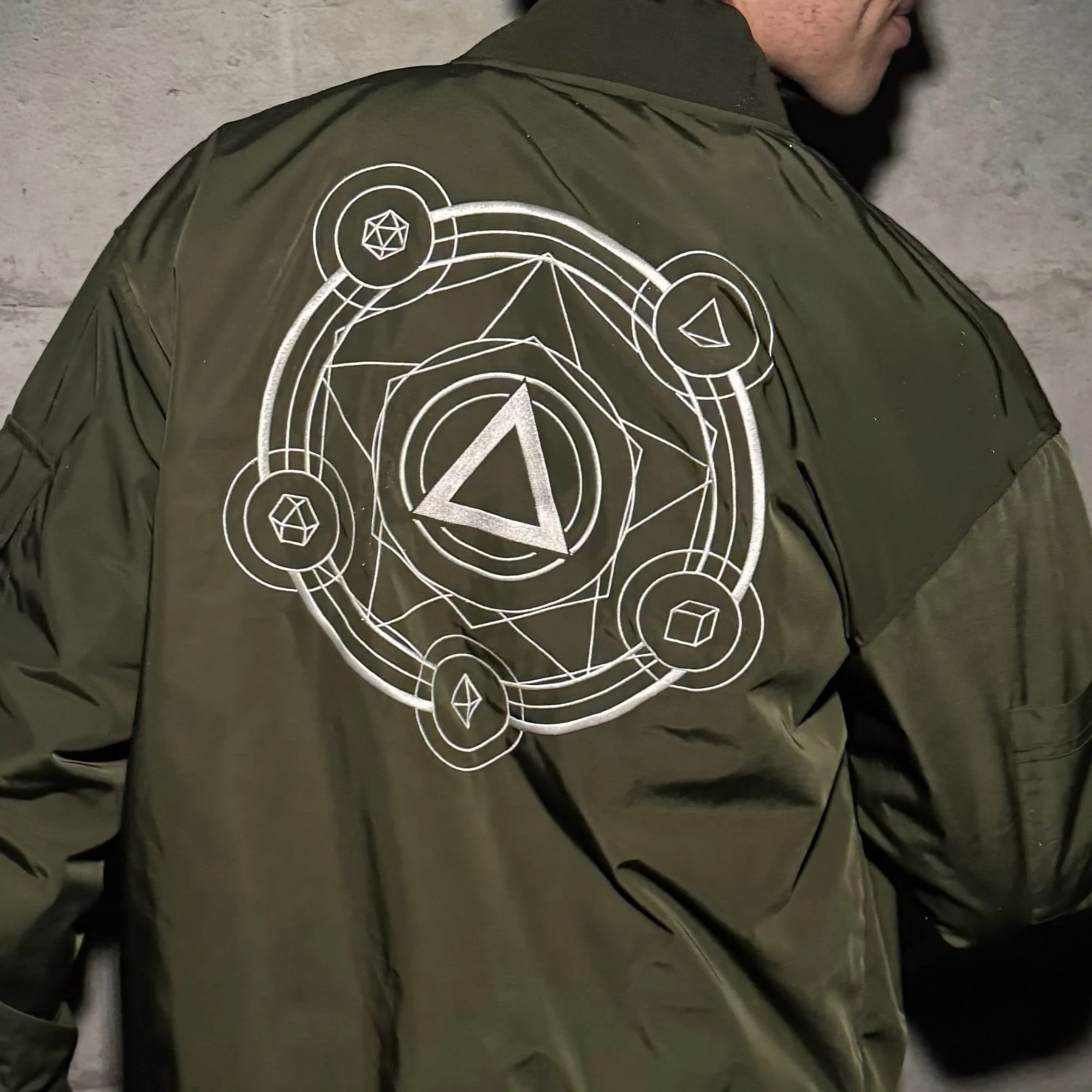 A person wearing a military green jacket with white geometric and circle designs on the back.