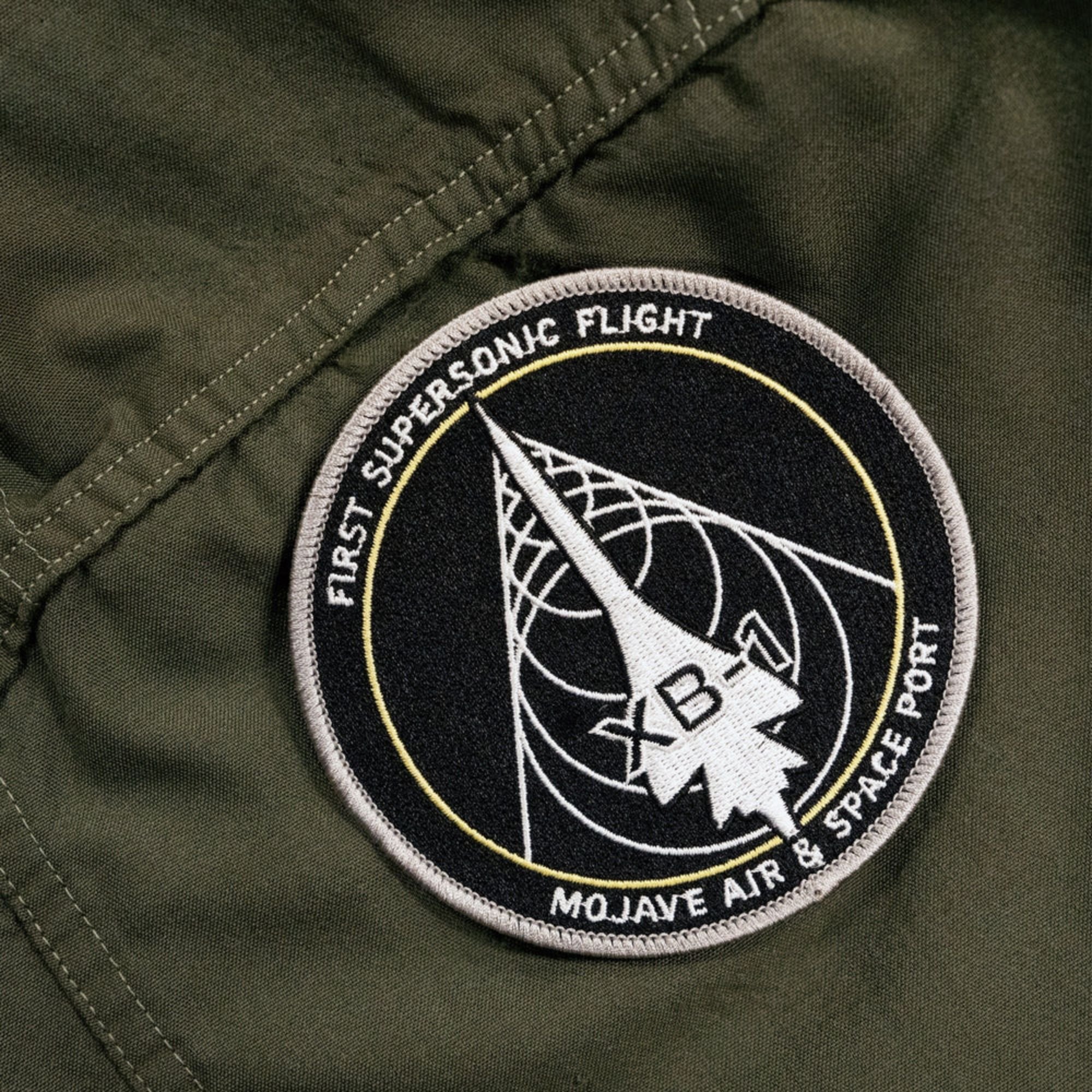 Close-up of a pvc patch sewn onto a dark green fabric with visible stitching.