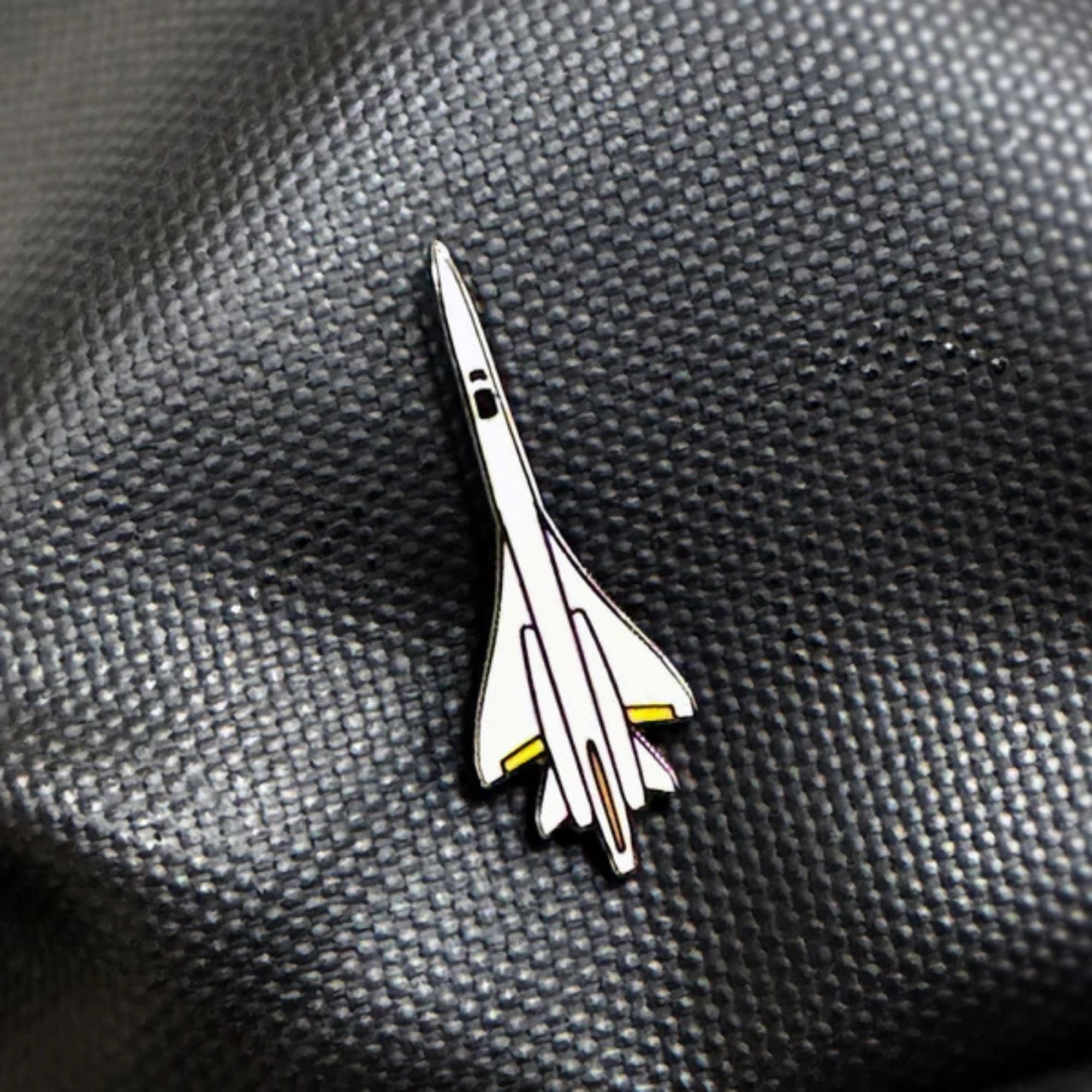 Close-up of a black textured surface with a small enamel rocket ship pin.