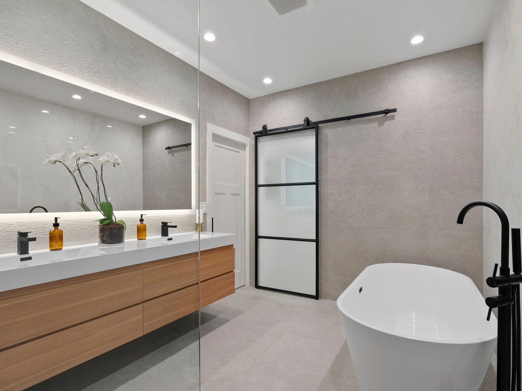 A custom bathroom cabinet in a modern style with white sinks as well as a large modern bathtub and glass plate door. Work completed by Valley Mill Shop.