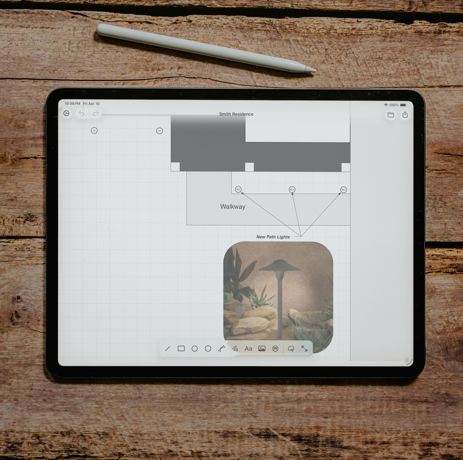 An iPad displaying a landscaping project plan with plant placement, walkway, and new path lights, placed on a wooden surface with a white stylus above it.