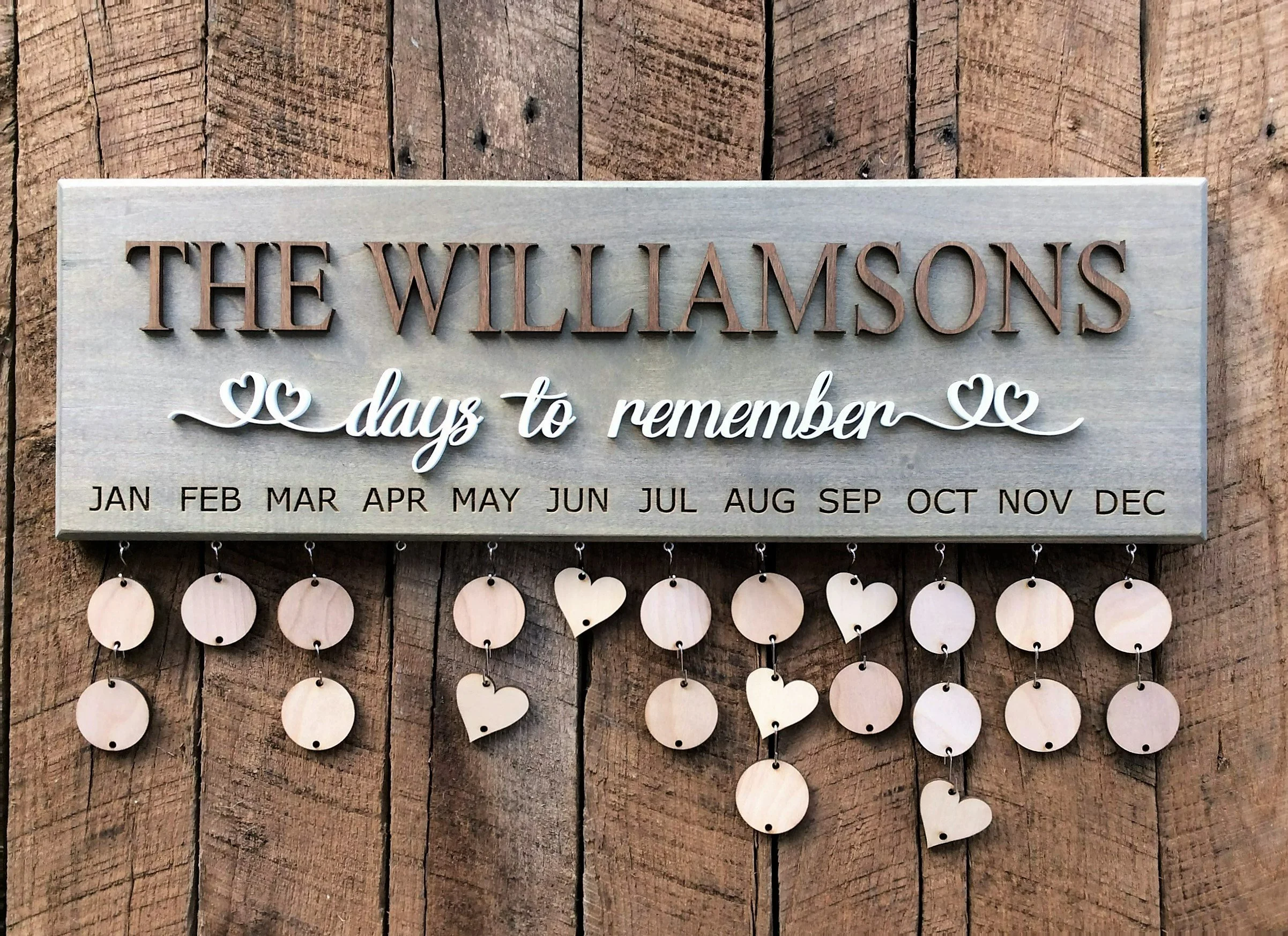 Wooden sign reads 'The Williamsons' with smaller text 'days to remember' and months listed below, on a wooden background.