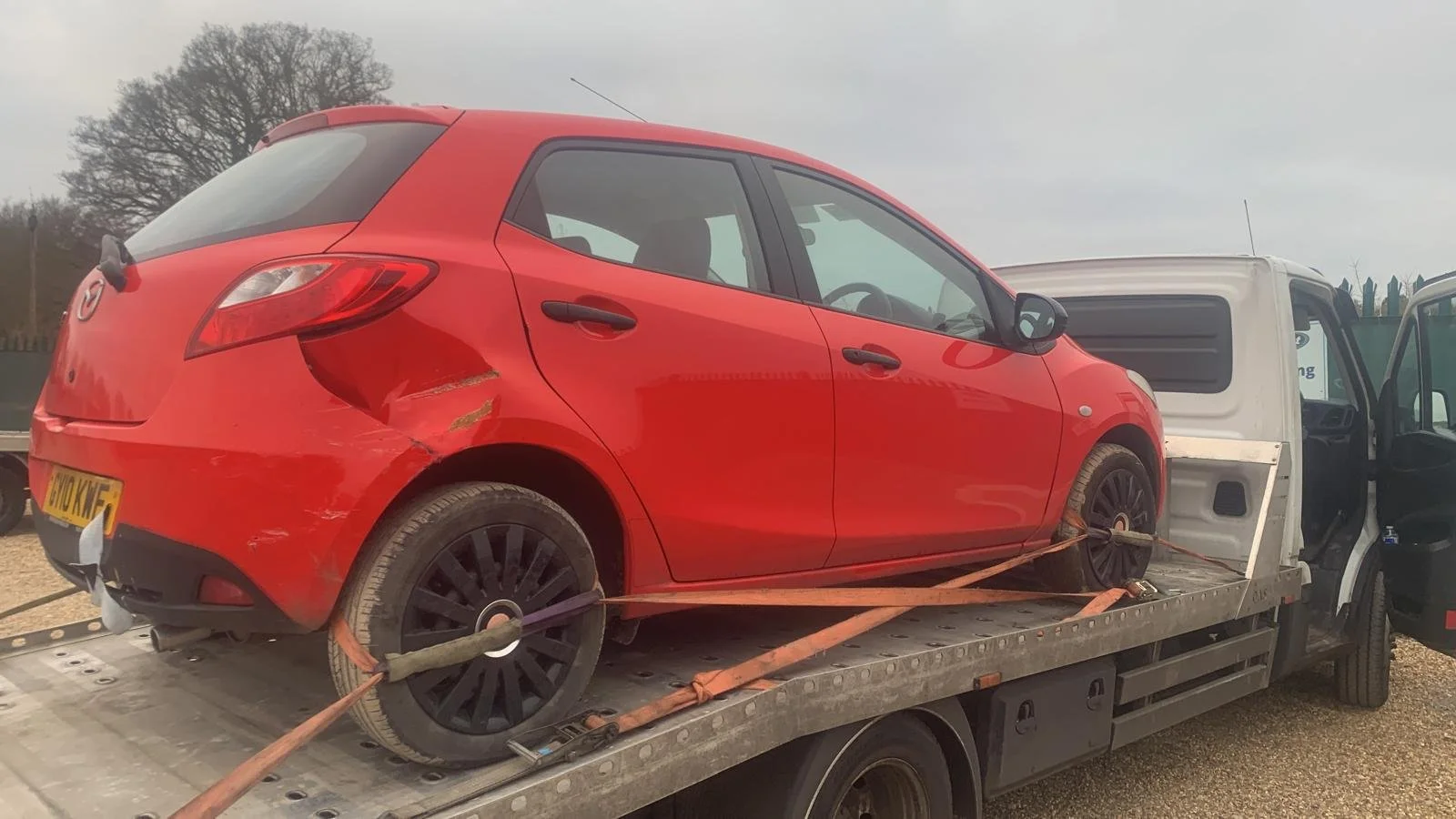 Red car secured on a flatbed tow truck with straps.
