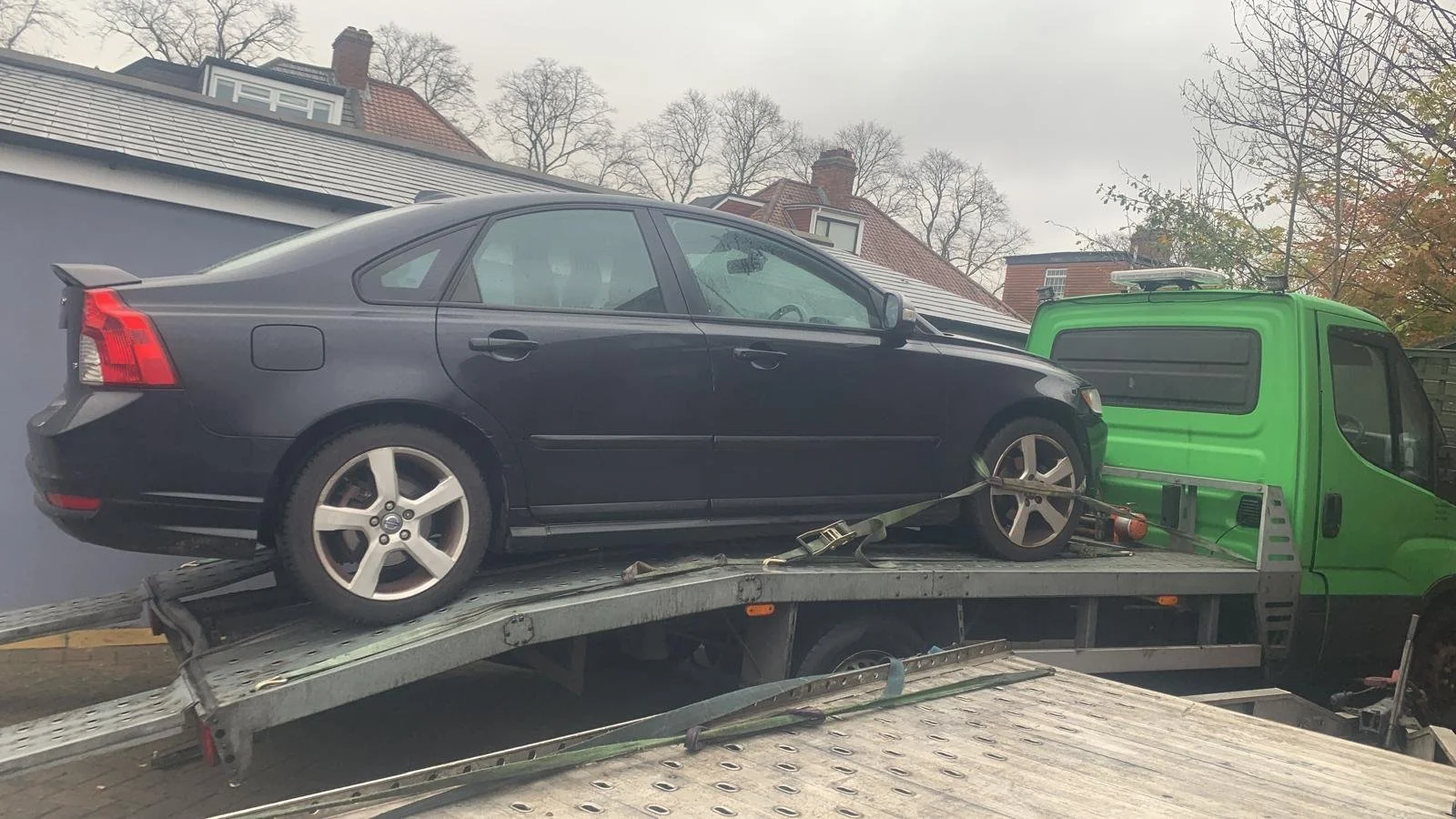 A black sedan car secured on a flatbed tow truck.
