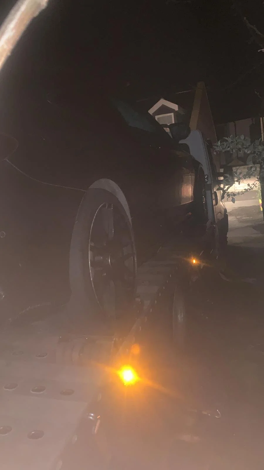 A black car loaded onto a flatbed tow truck at night, illuminated by the truck's lights.