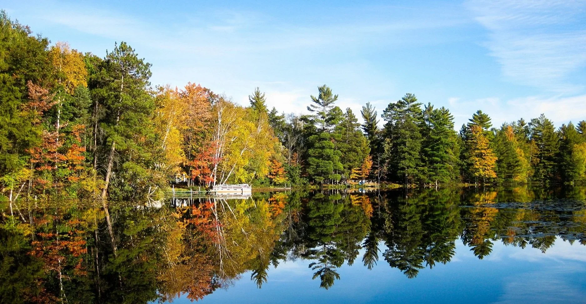 Calm lake reflecting colorful autumn trees and blue sky.