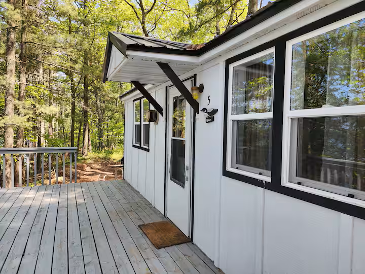 Outdoor view of a white house with black trim, a small deck, and surrounded by trees in a forested area.