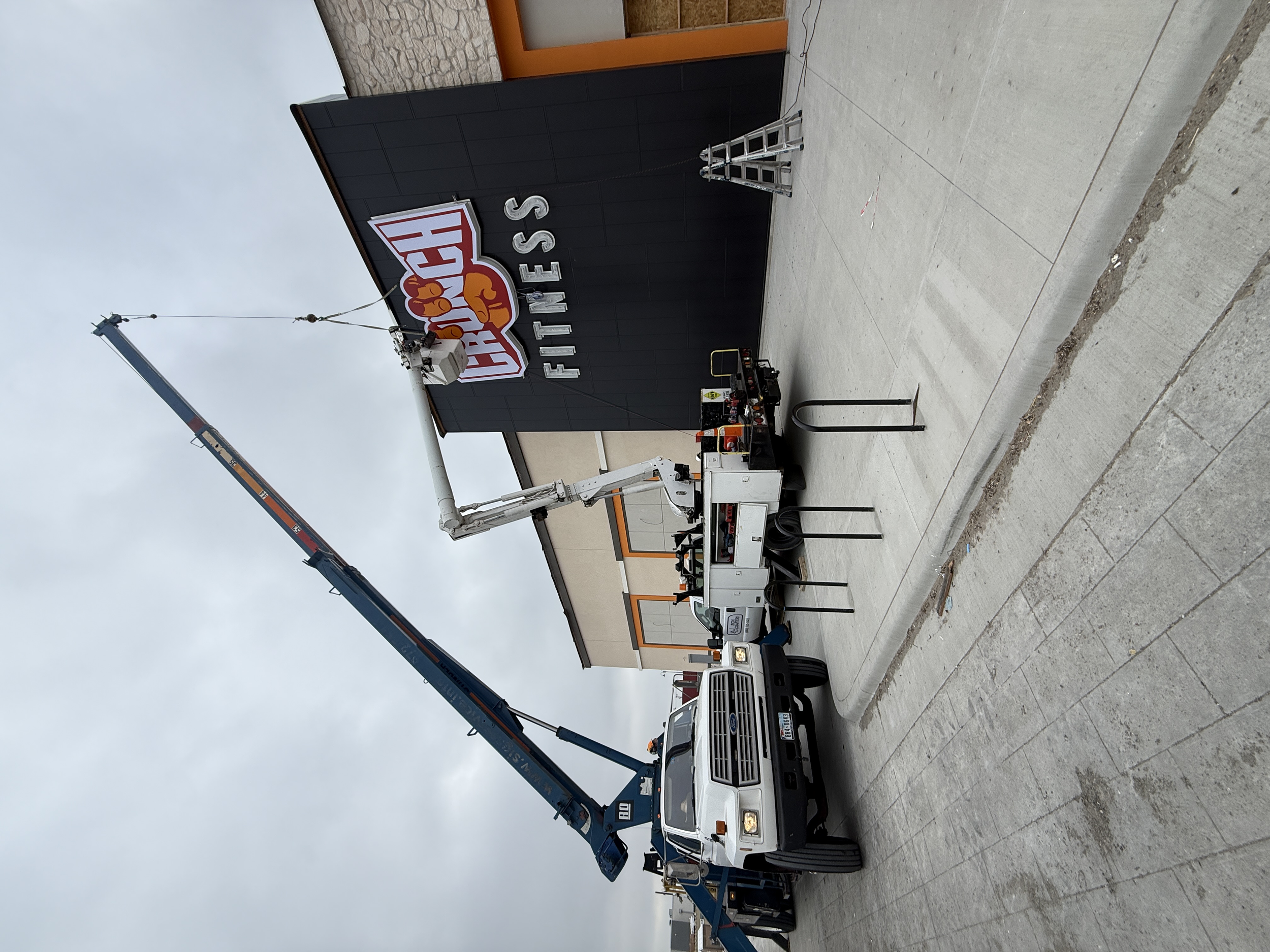 A pick-up truck with a crane lifting huge custom LED sign, And sign installers installing it.