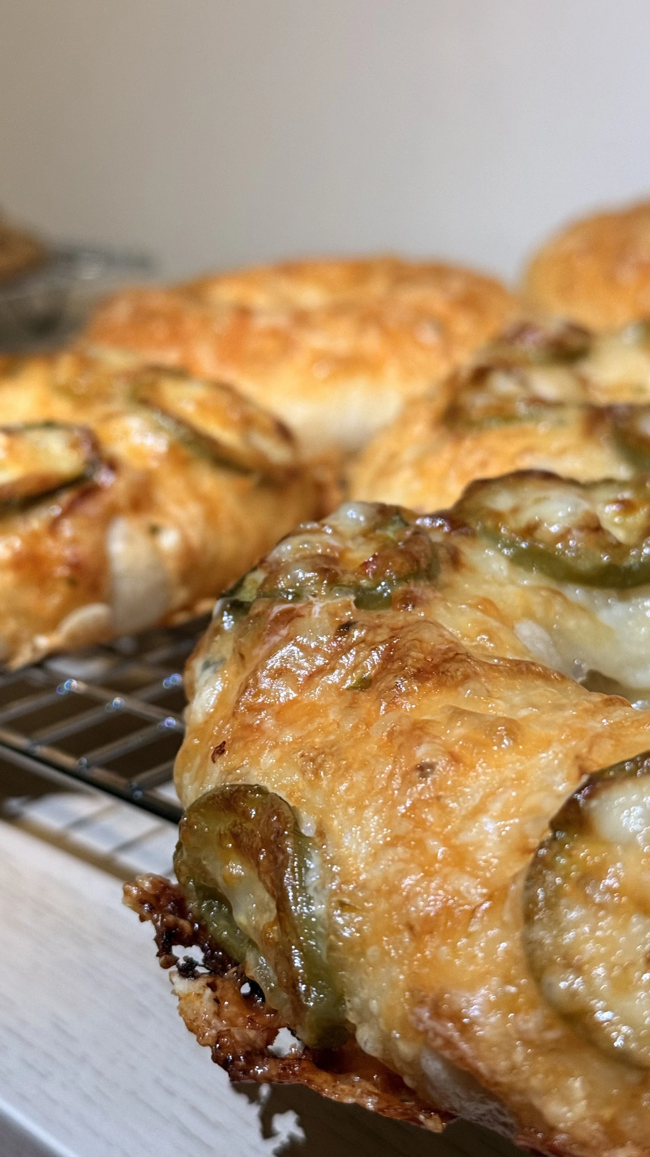 Baked chicken breast topped with melted cheese, green chili slices, and herbs, placed on a wire rack.