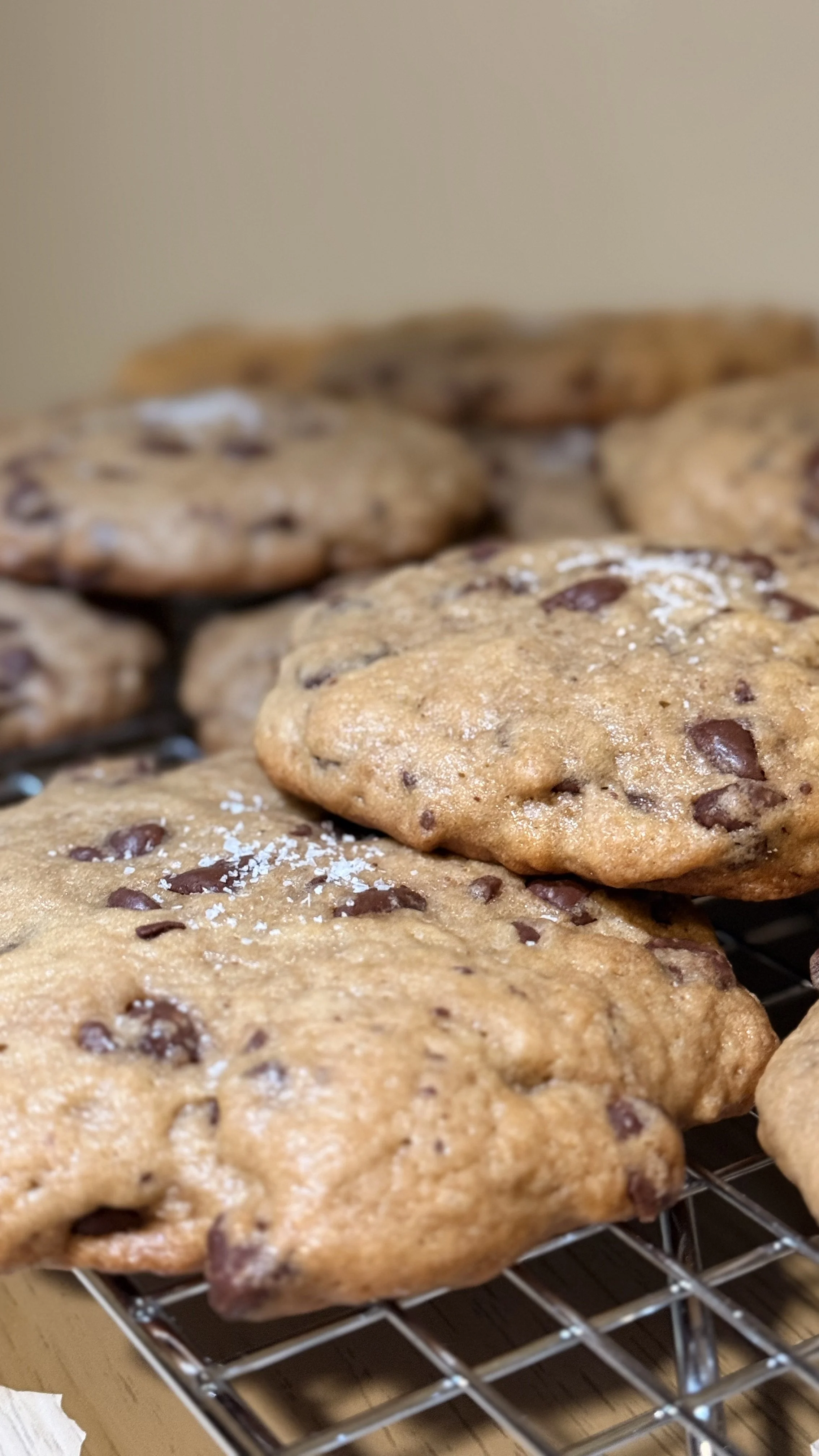 Close-up of freshly baked sourdough chocolate chip cookies on a cooling rack, sprinkled with a light dusting of salt.