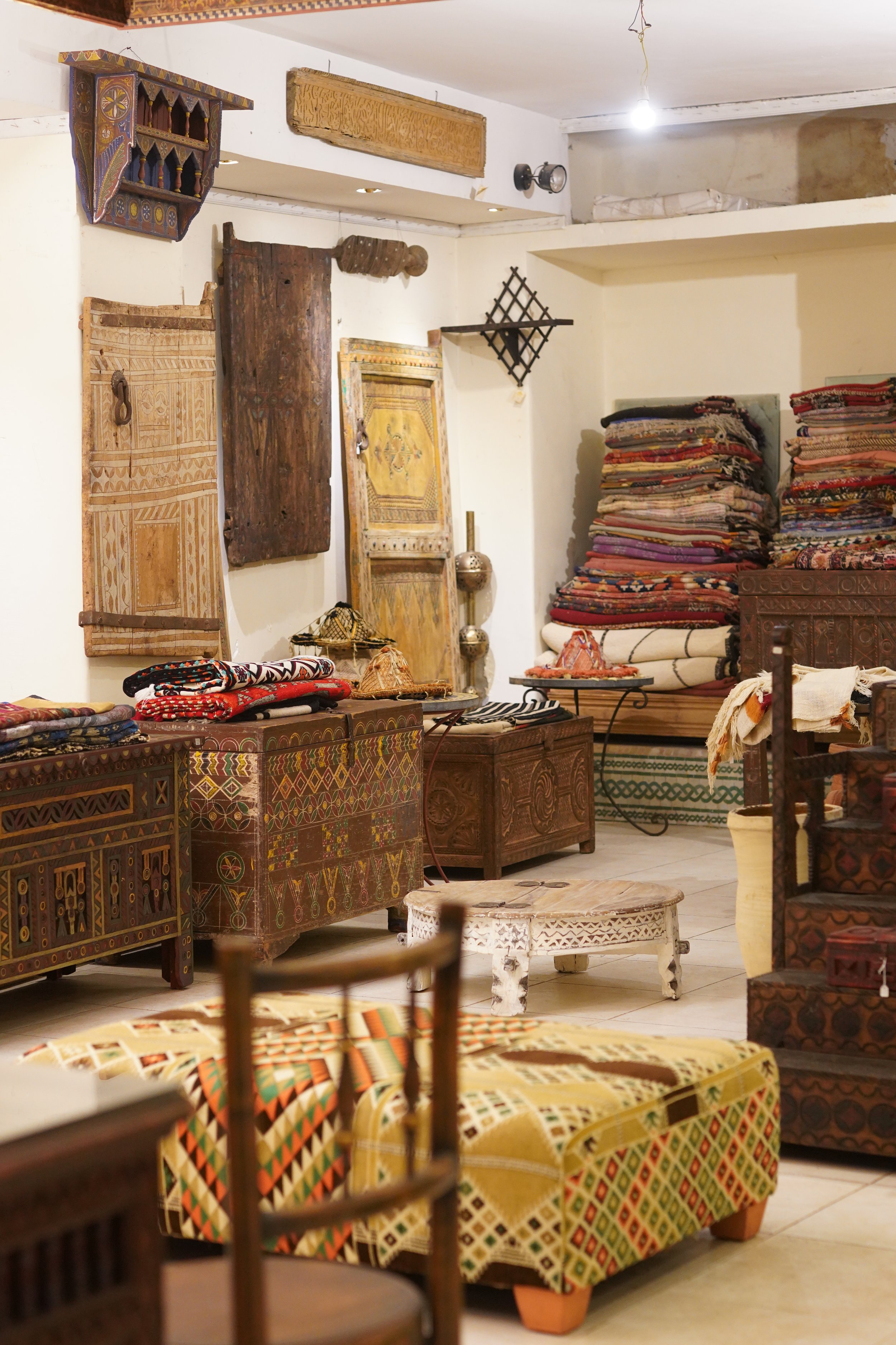 Intérieur d'un magasin vendant des meubles et des textiles traditionnels, avec des meubles en bois sculpté, des tissus colorés empilés et des objets décoratifs.