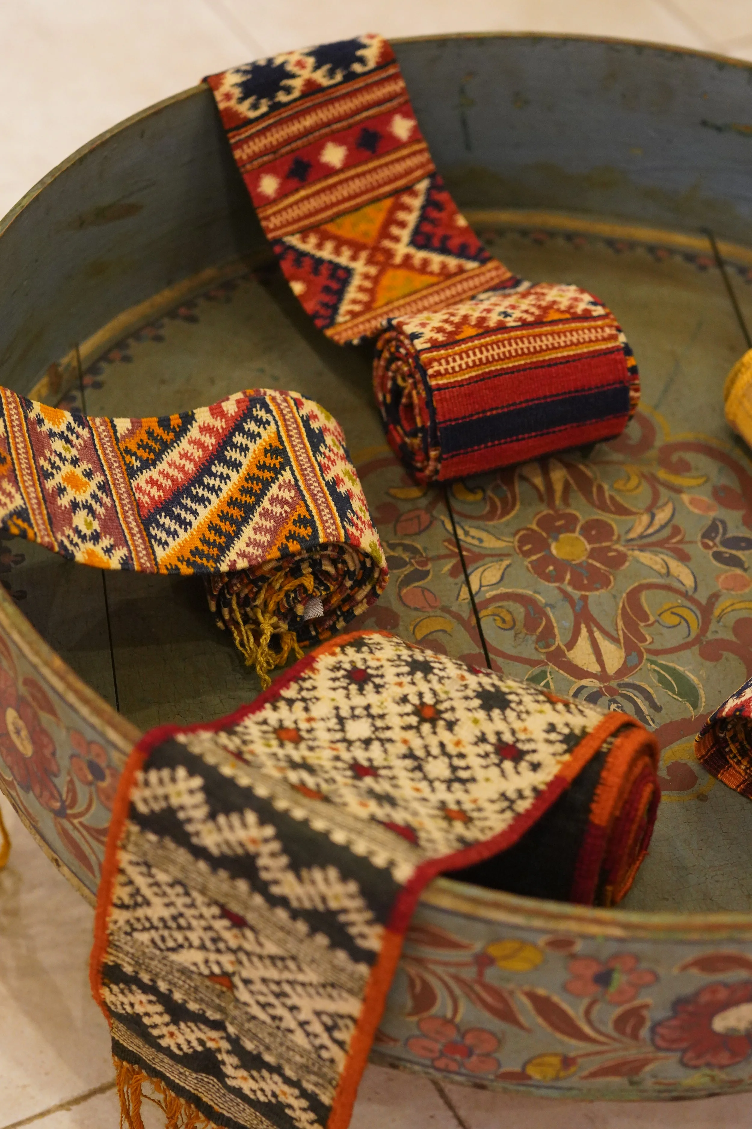 Écharpes tissées aux motifs géométriques colorés, drapées sur le bord d'un grand bol décoratif en céramique avec des motifs floraux.